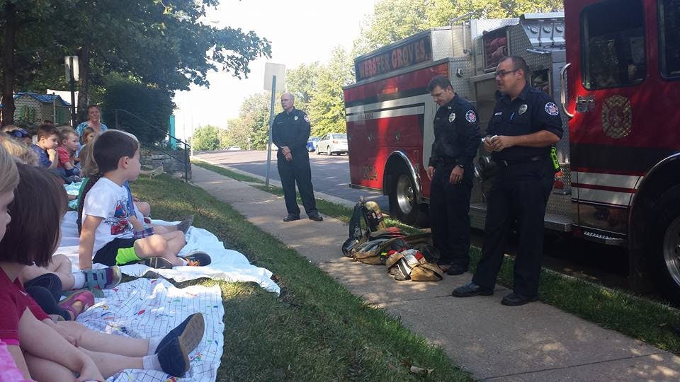 People in uniform standing by a fire truck with children sitting on blankets