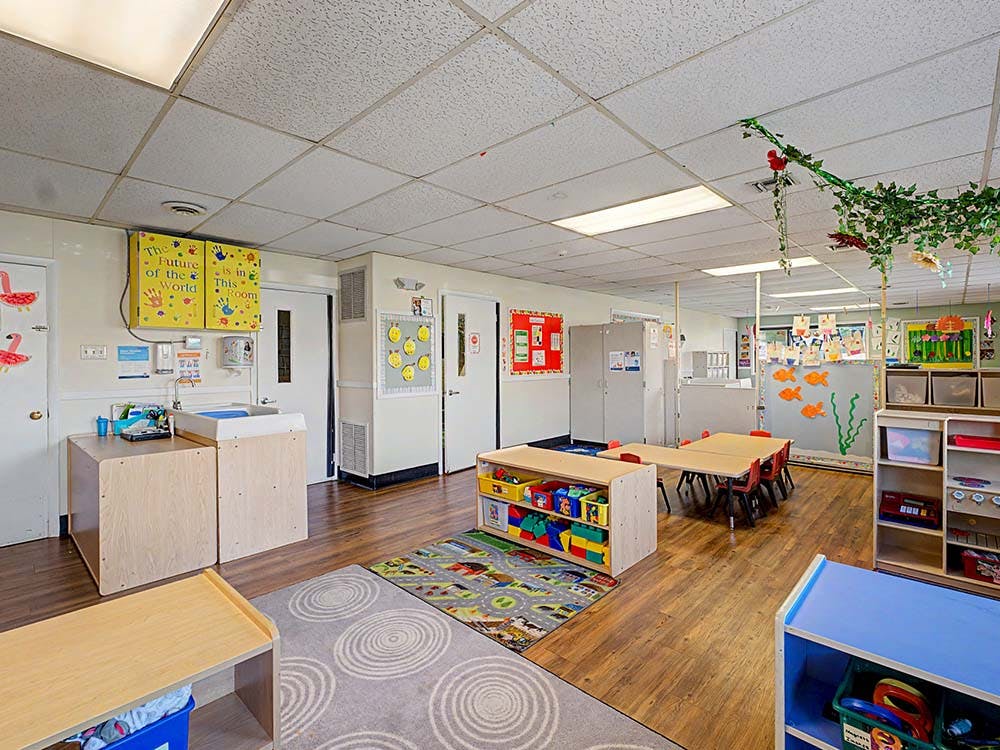 An empty childcare room with small tables, play mats, and a changing station