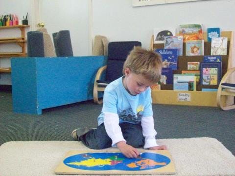 Child kneeling on floor playing with a world map puzzle