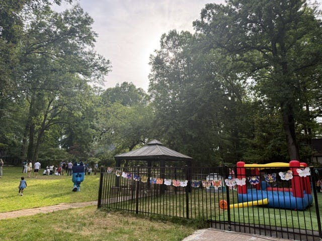 People gathered in a grassy park with a gazebo and a bounce house