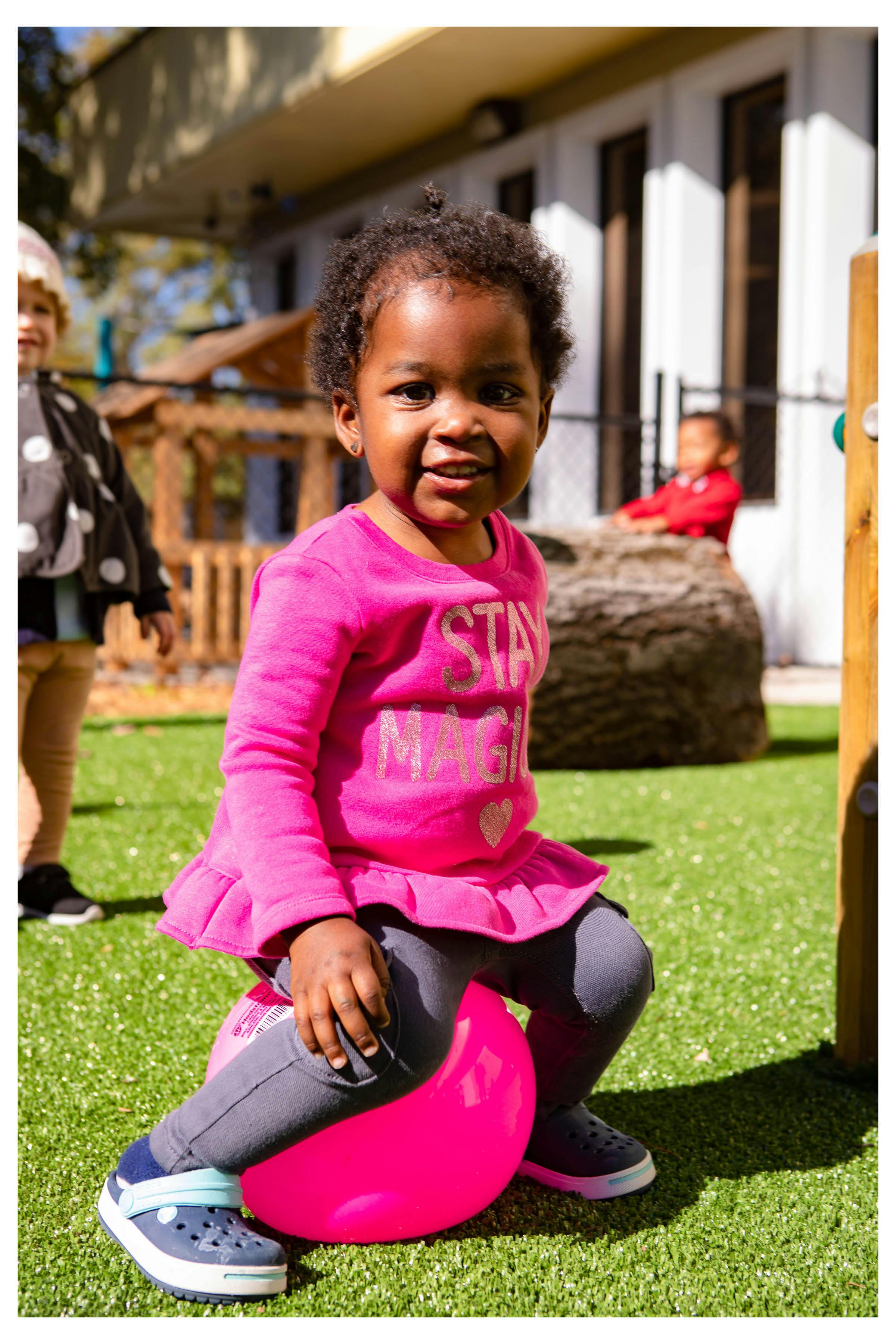 Child sitting on a pink ball on artificial grass