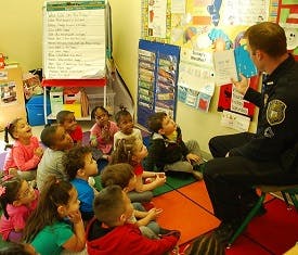 Person in uniform speaking to a group of children in a classroom