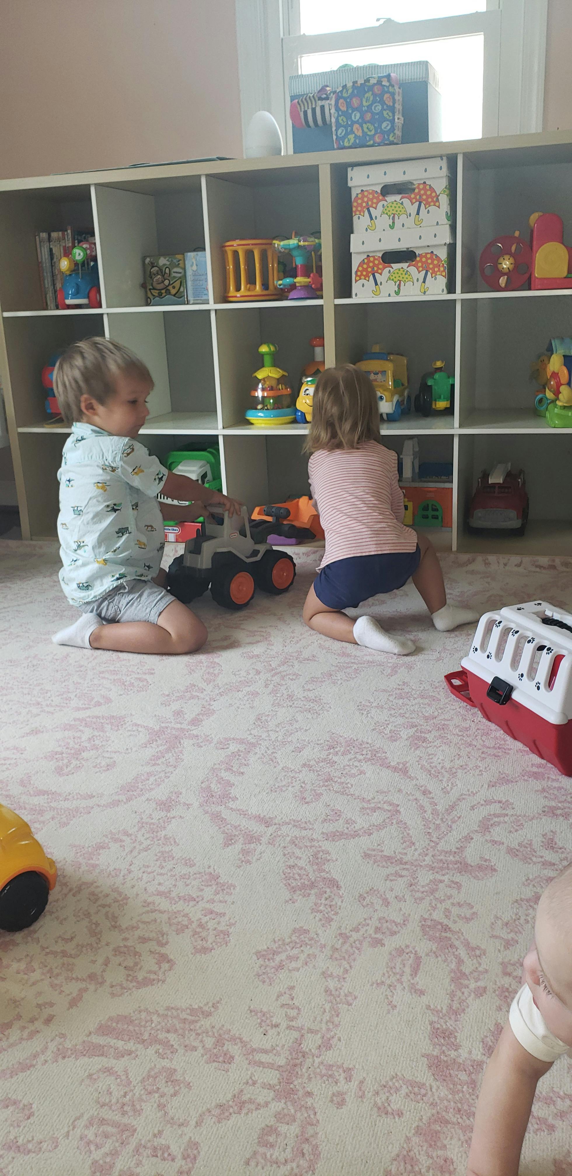 Two children playing with toys on the floor in a room with shelves