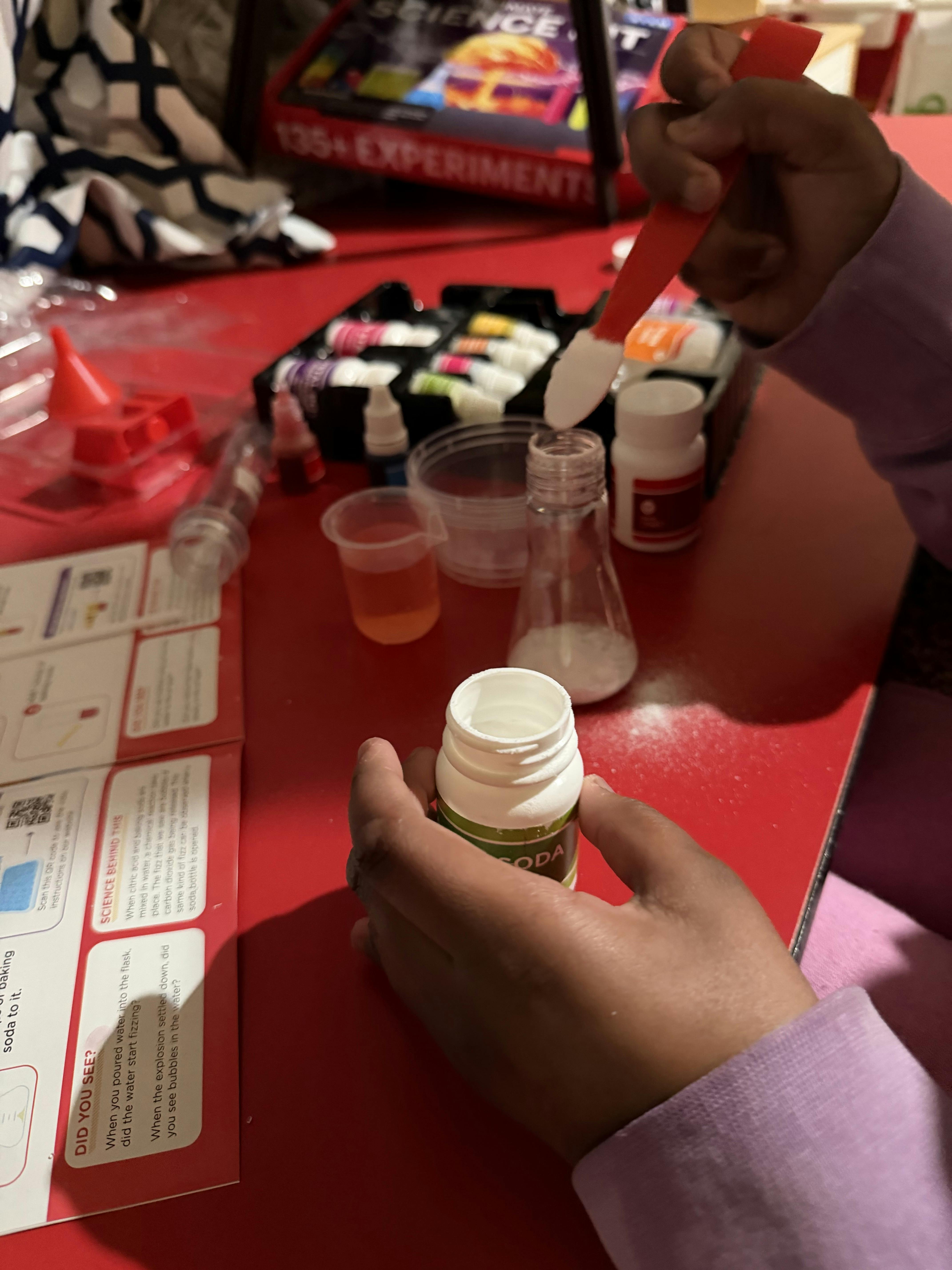 Child adding white powder to a flask with a spatula