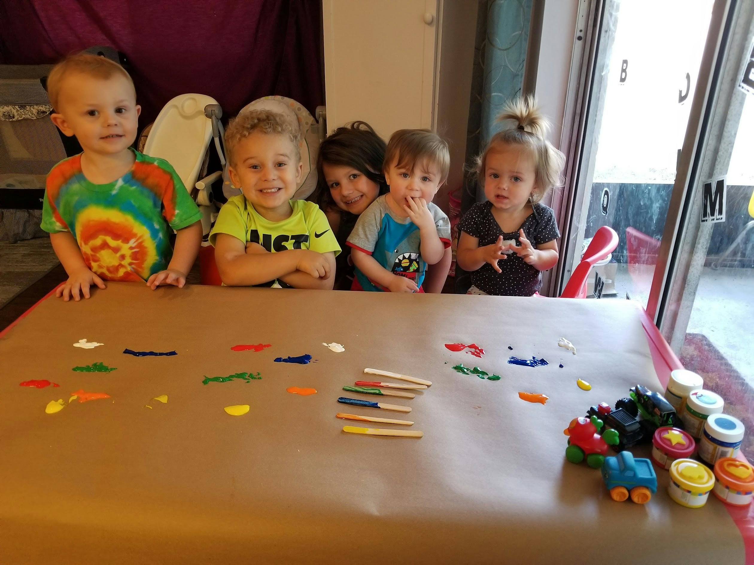 Five children standing behind a table with paint and craft sticks