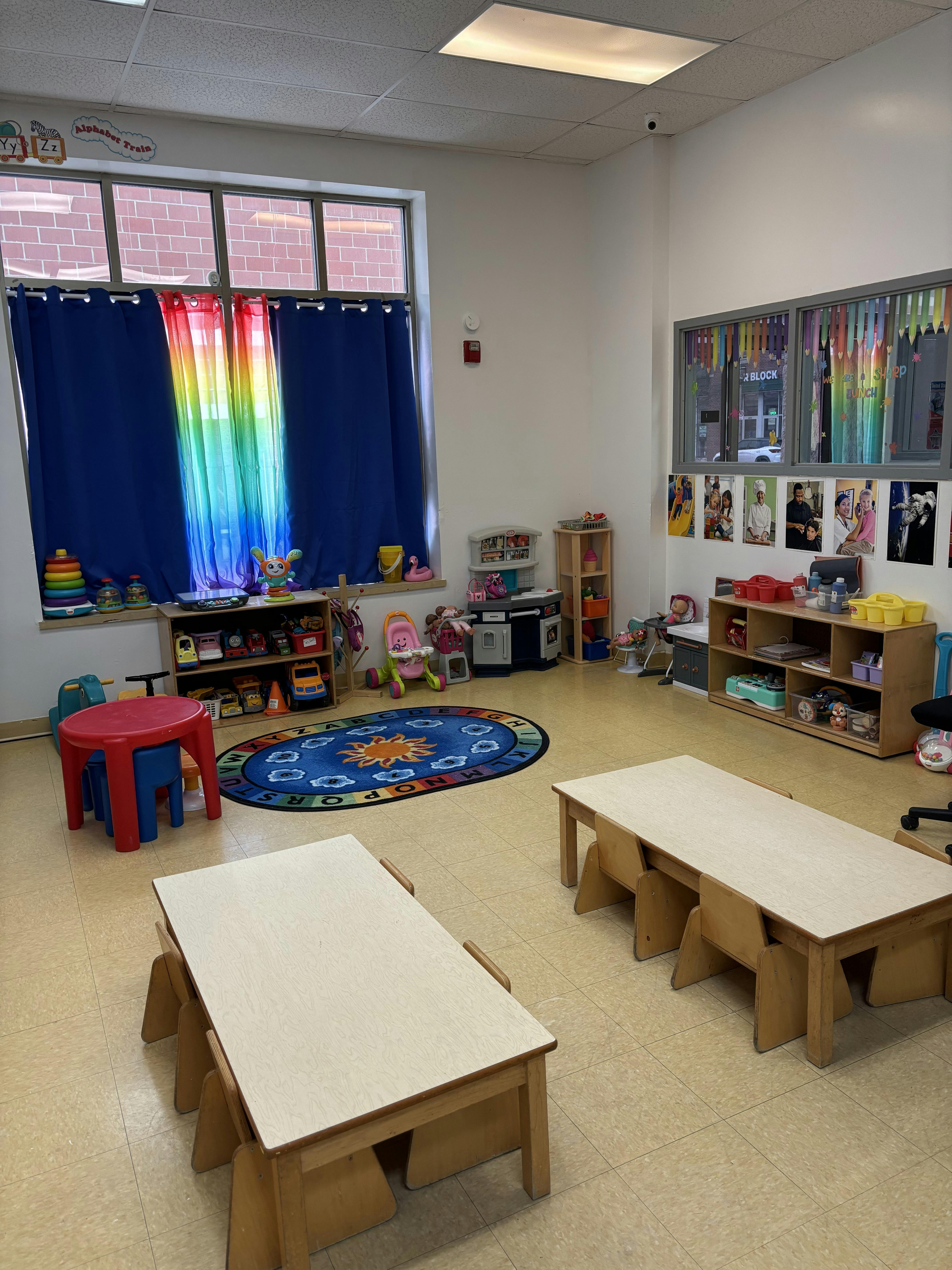 A colorful empty classroom with small tables and chairs, toys, and an alphabet rug