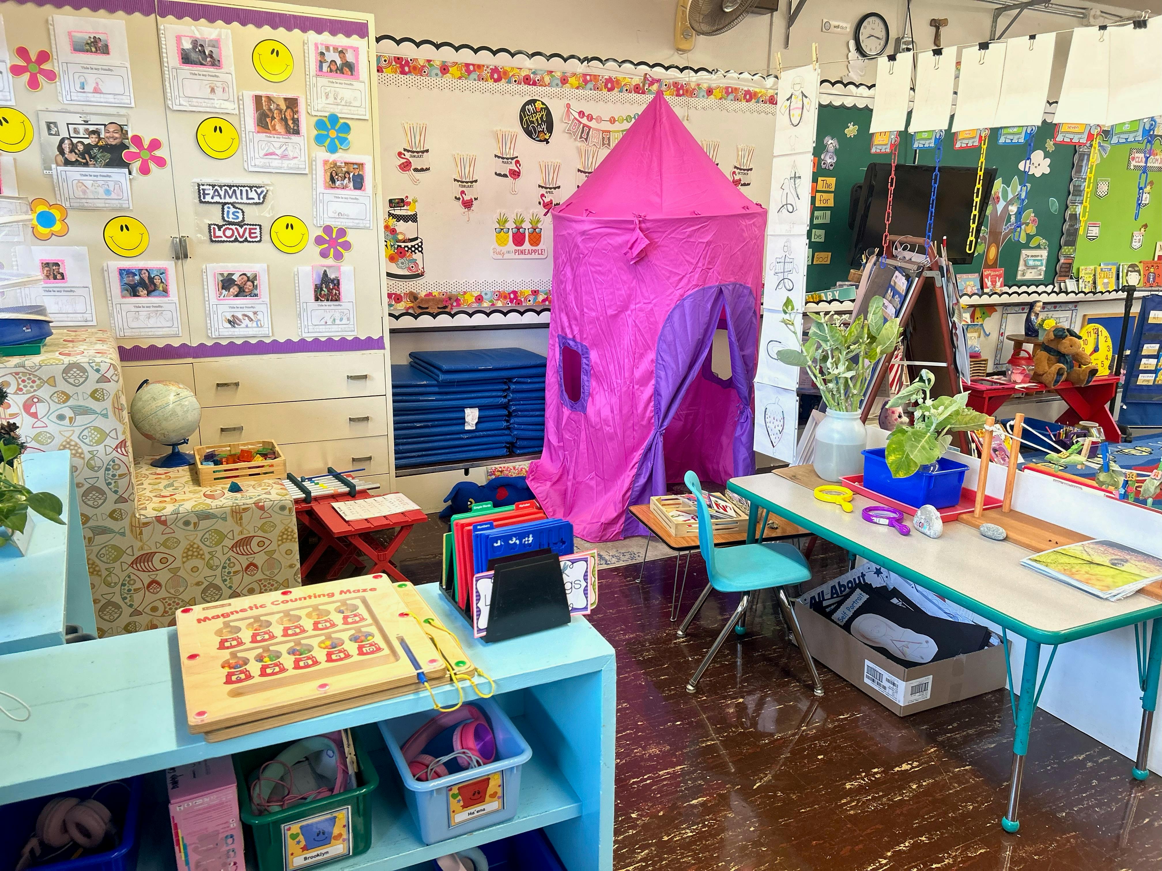 Classroom with a pink play tent, tables, and shelves with learning materials
