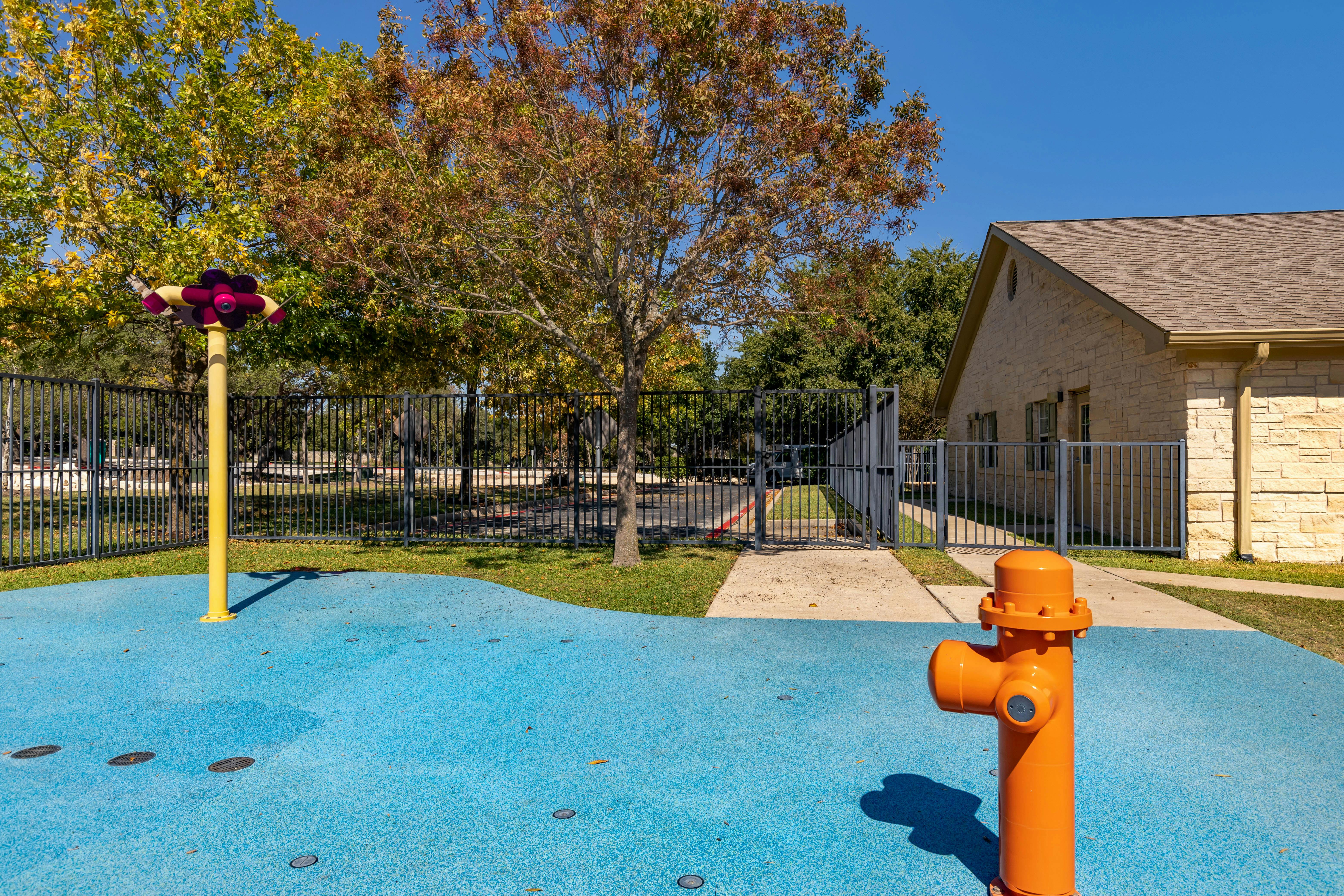A spray ground with a yellow post water feature and an orange fire hydrant-like sprayer