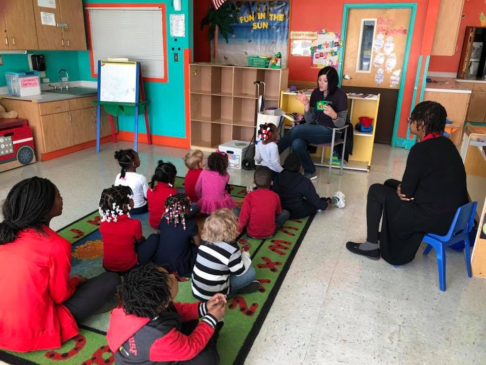 Adults and children sitting on a rug in a classroom