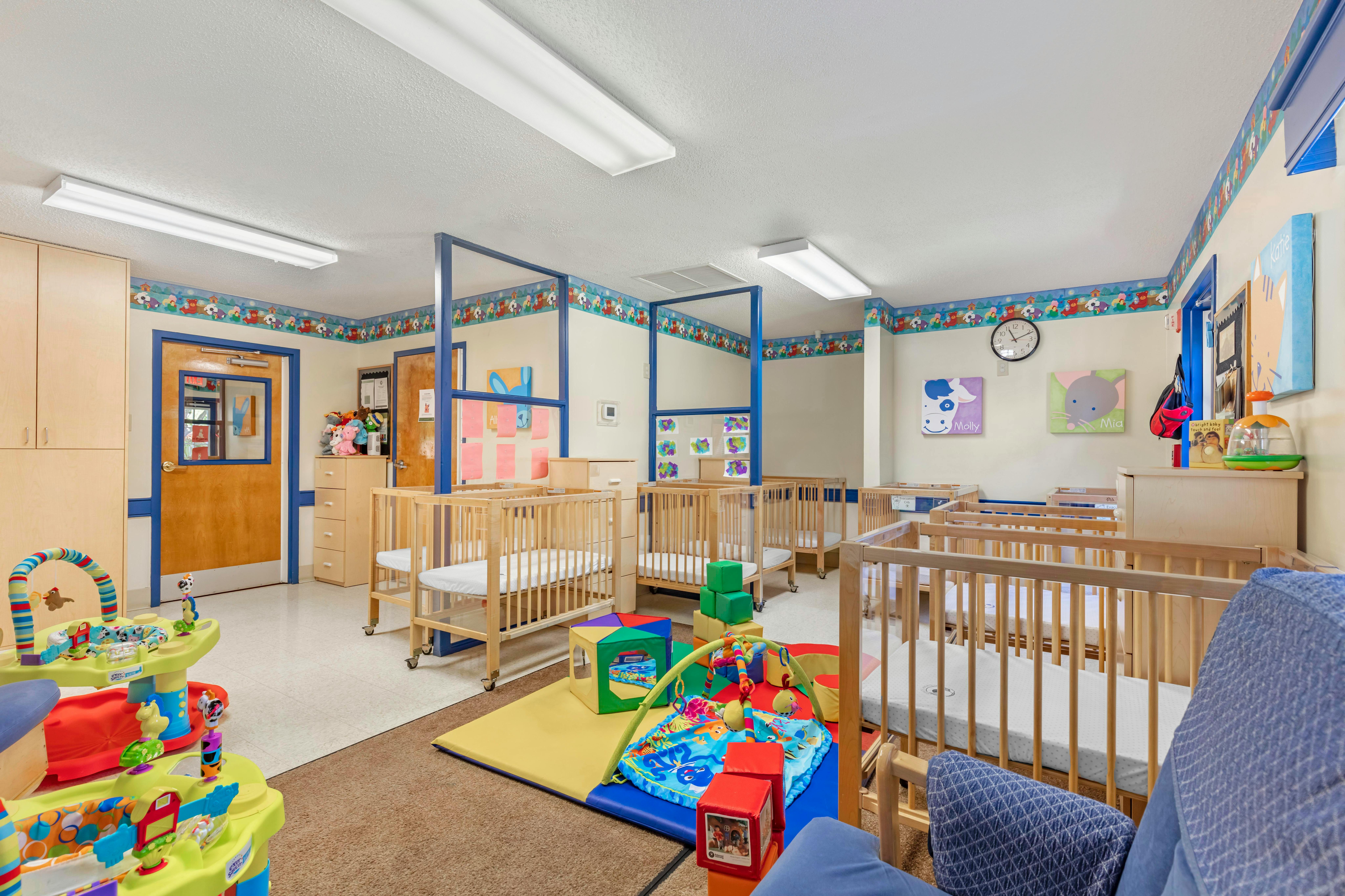 A room with several wooden baby cribs and play areas with colorful toys