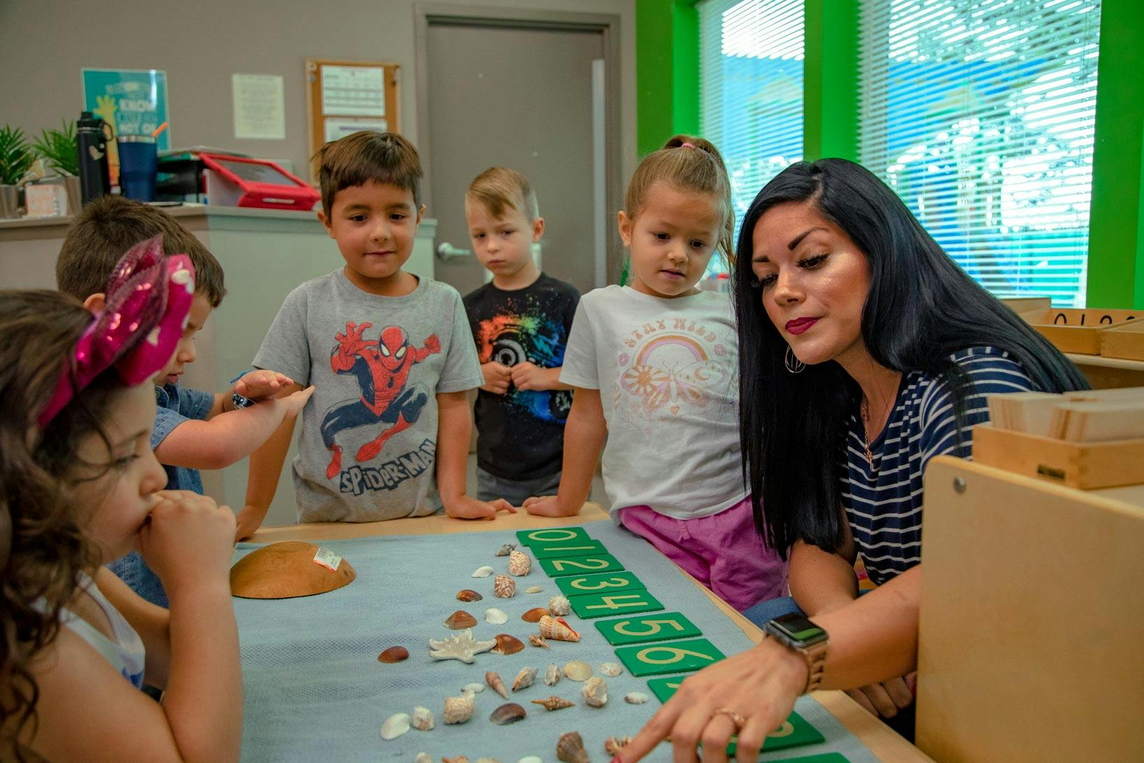 Adult and children in a classroom looking at seashells on a numbered mat
