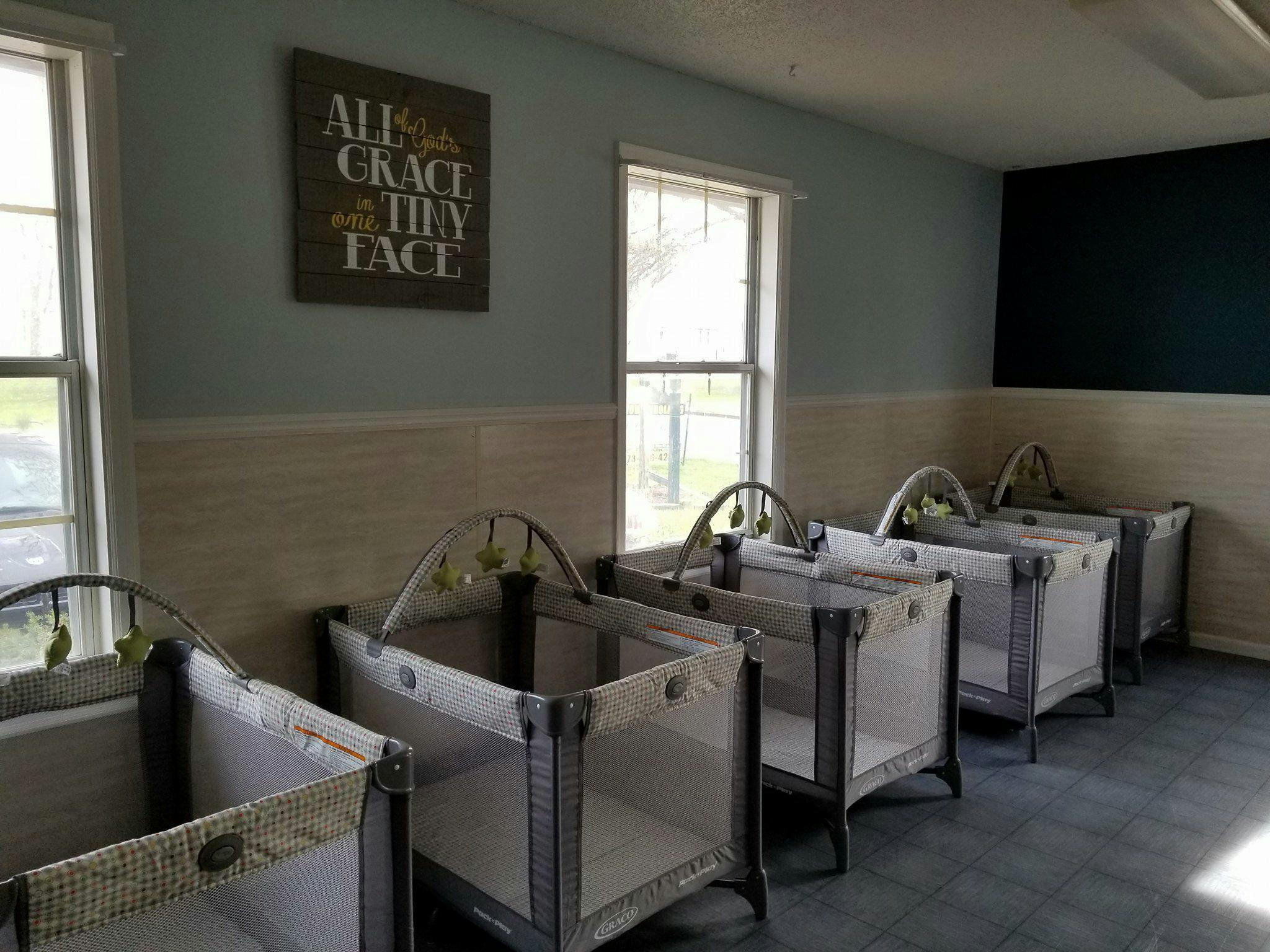 Row of empty cribs in a room with windows