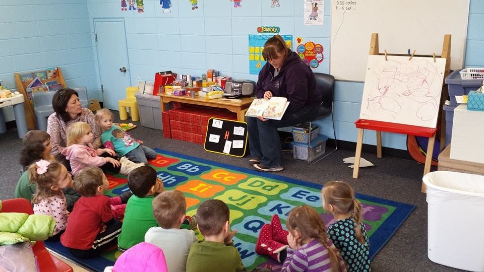 Two people reading to a group of children in a classroom