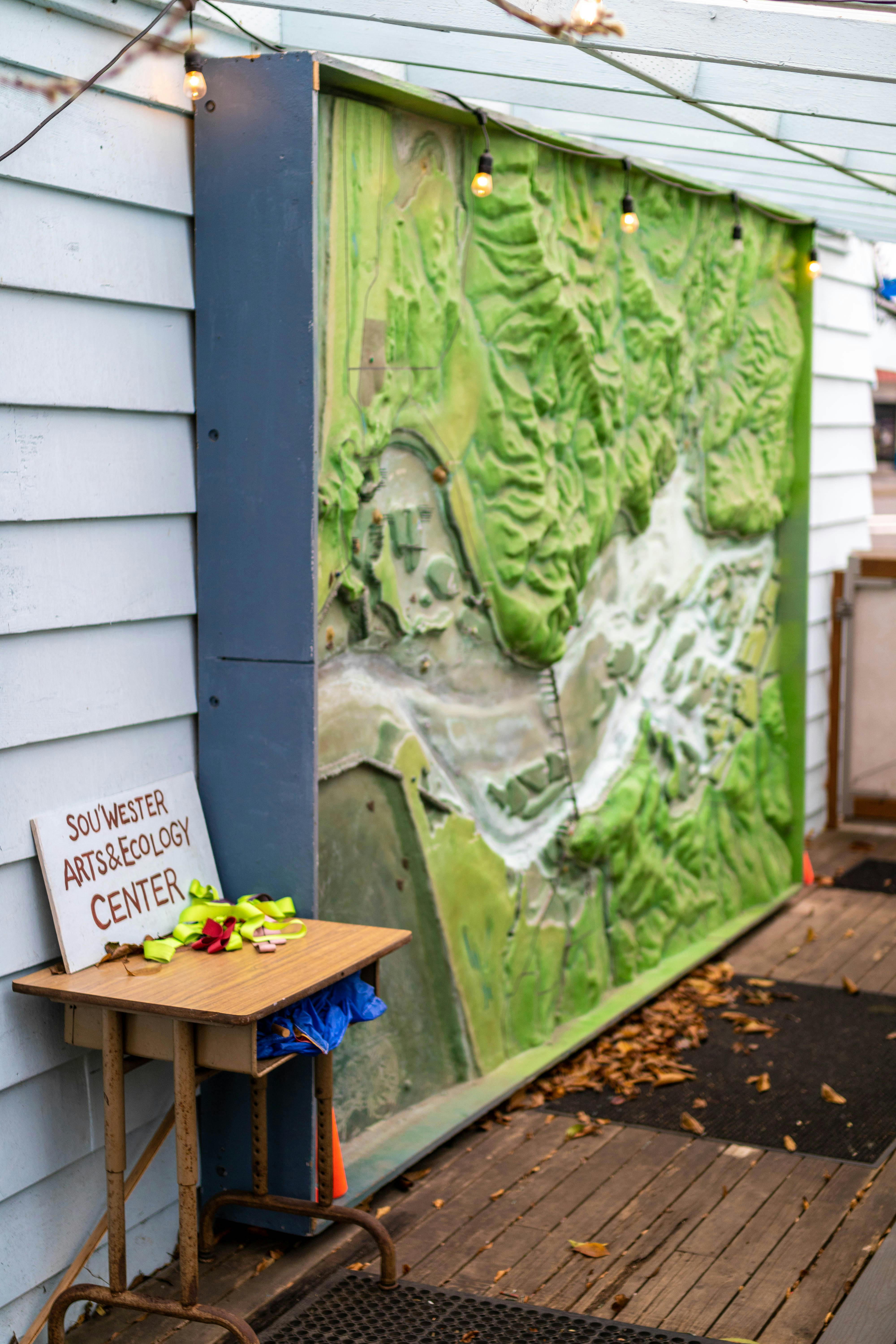 A large green topographical map next to a small table with a sign