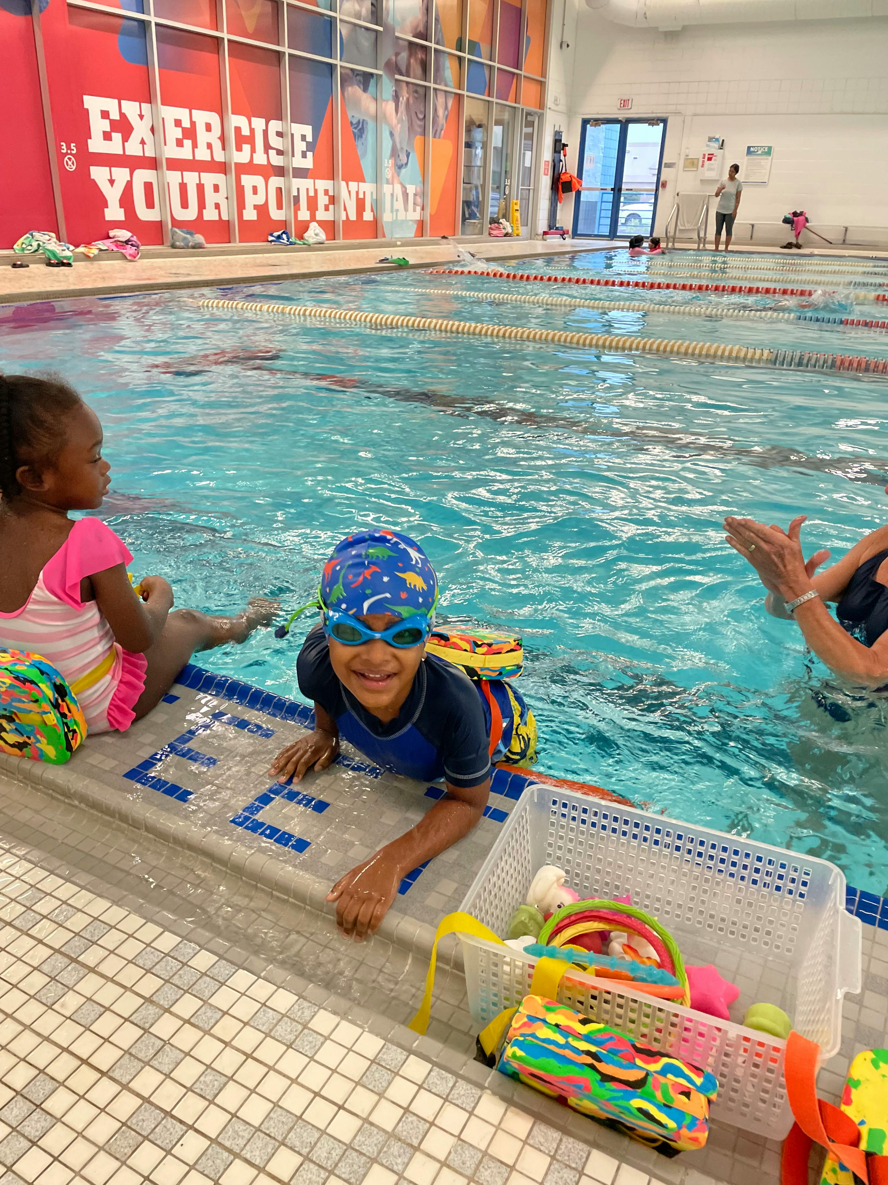 Child in swim cap and goggles at the edge of a swimming pool