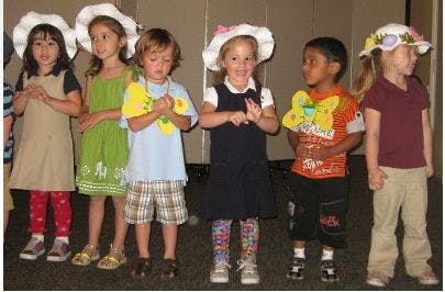 Six children wearing hats and holding paper cutouts