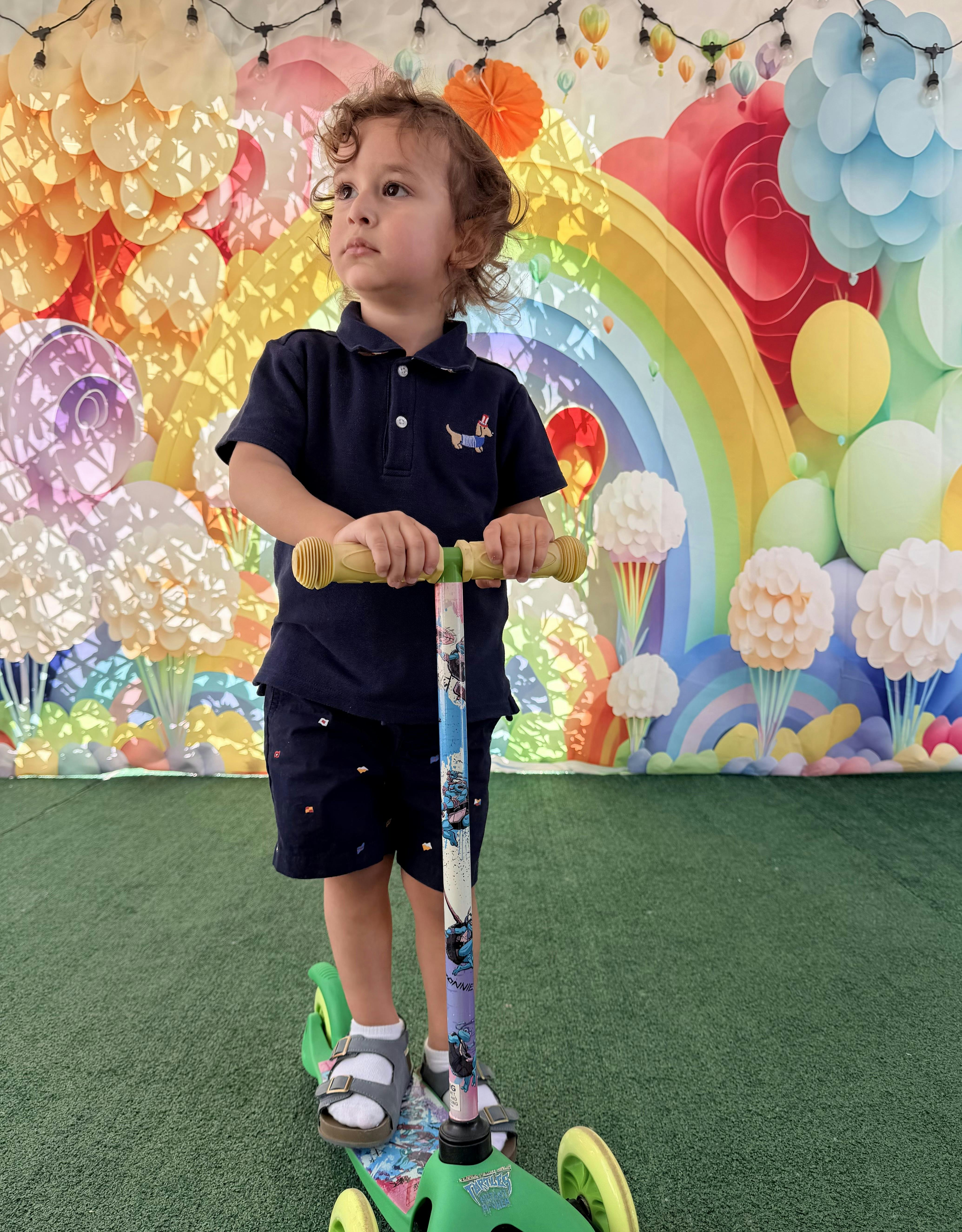 Child standing on a kick scooter in front of a rainbow backdrop