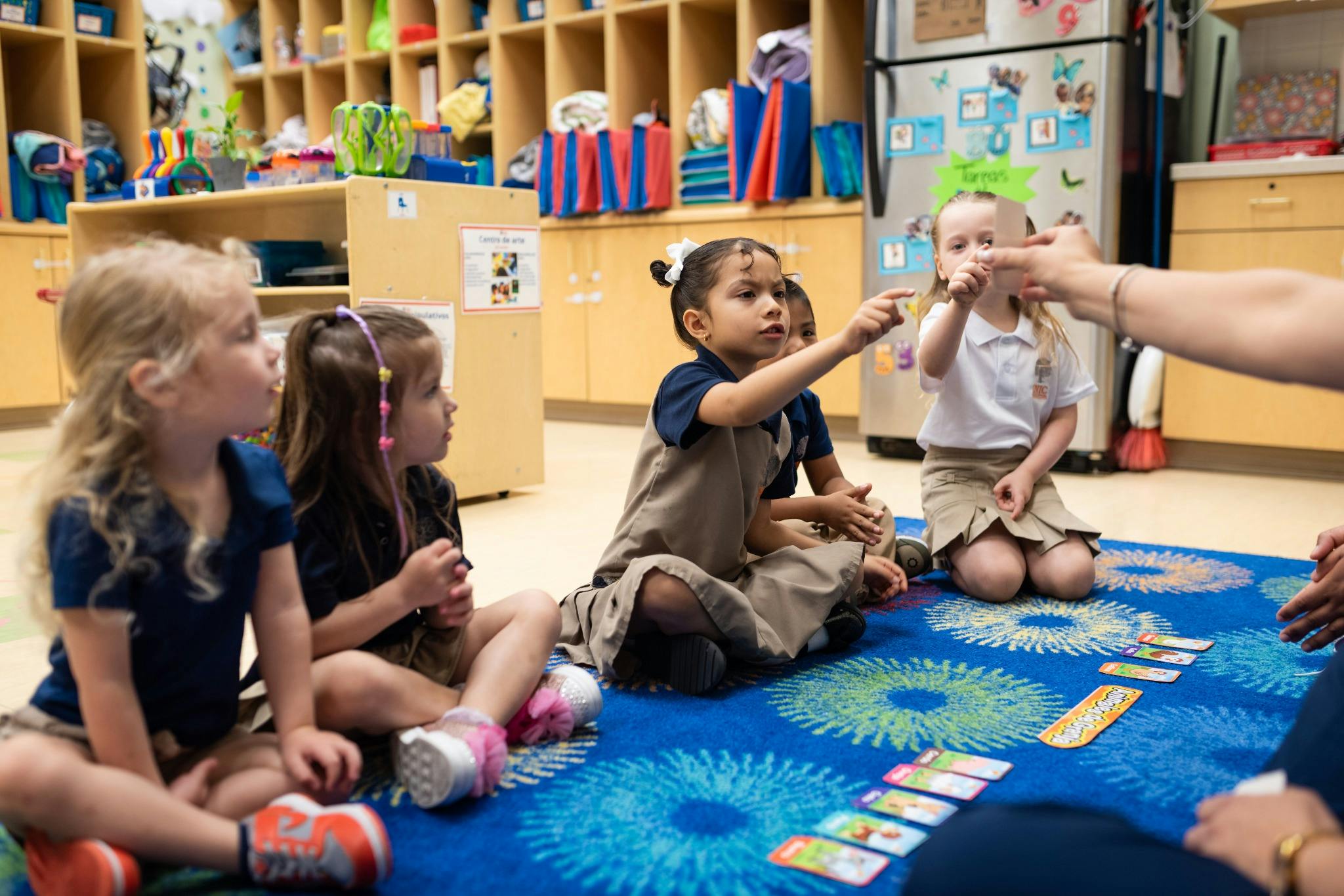 Several children sitting on a rug in a classroom, one child pointing