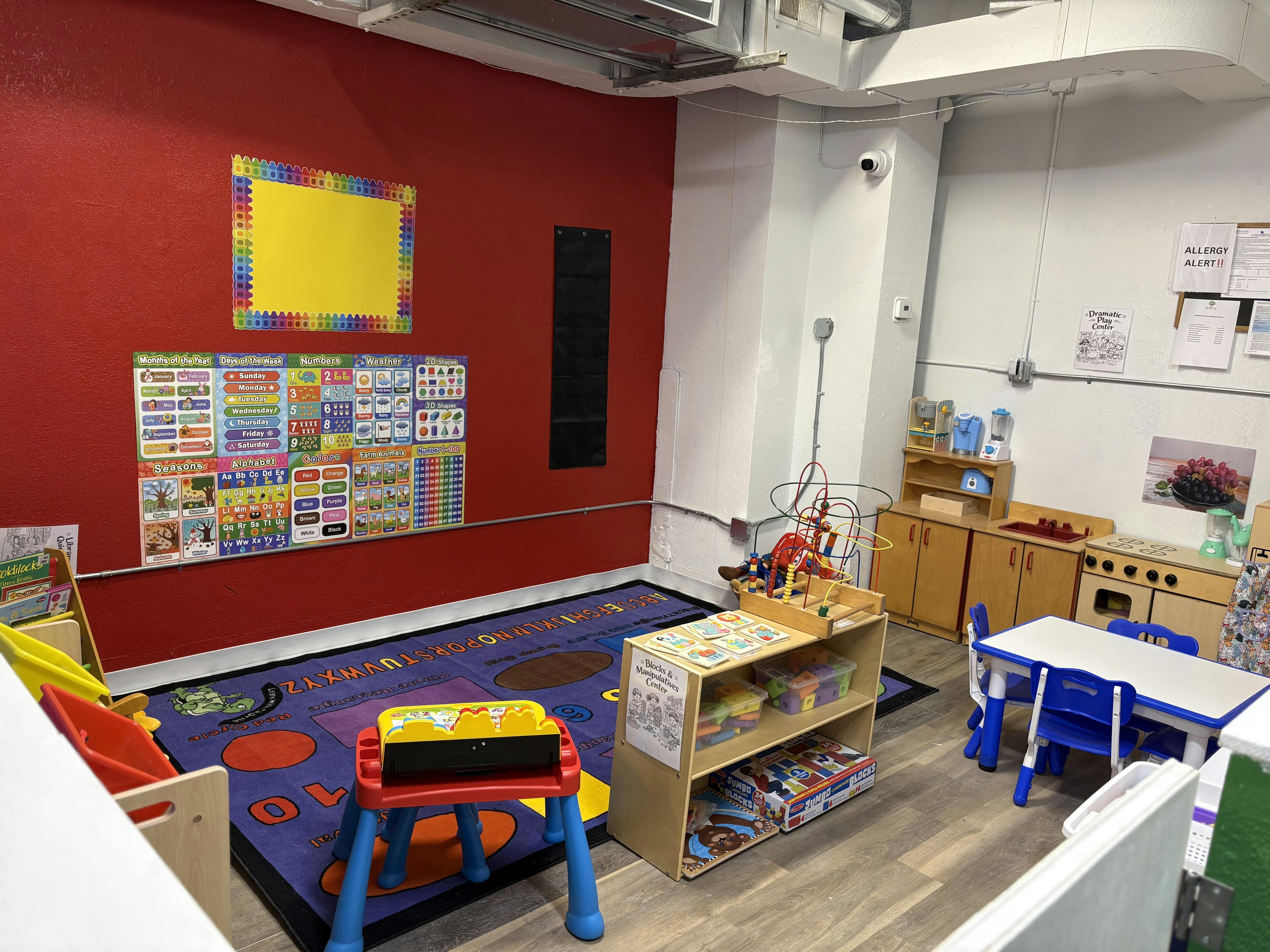 Classroom with educational posters, alphabet rug, small table and chairs, and play kitchen