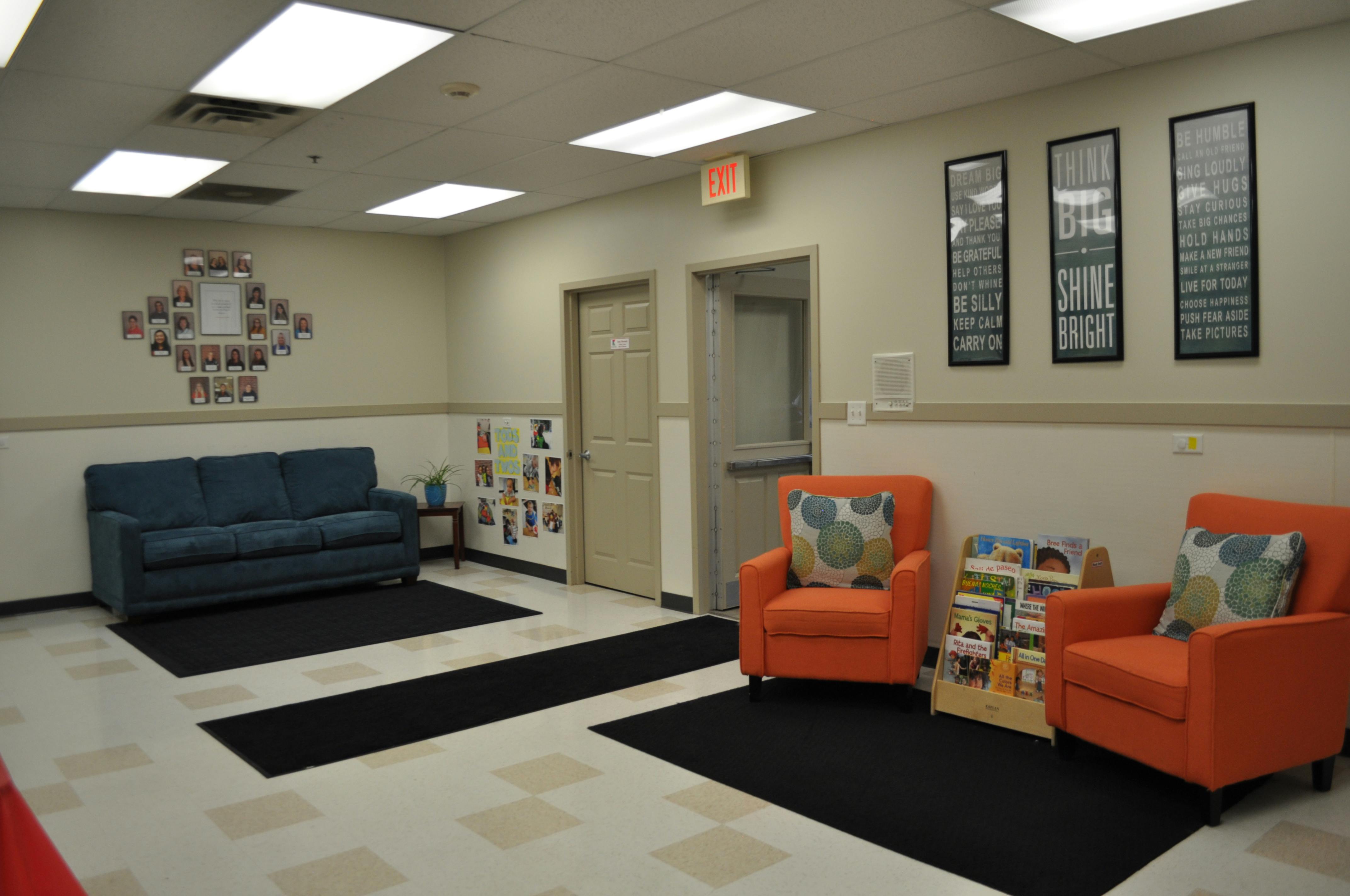 Lobby with a blue couch, two orange armchairs, and framed motivational posters