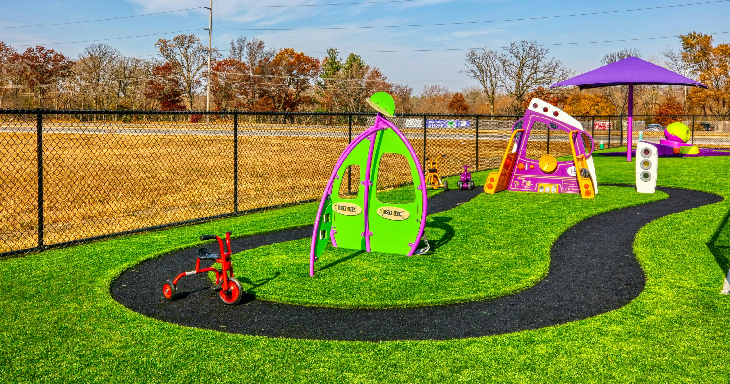 Colorful playground with green turf, purple play structures, and a red tricycle