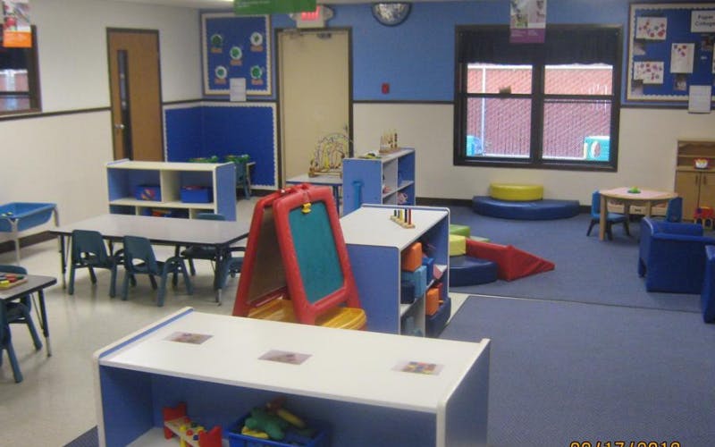 A colorful empty classroom with small tables, chairs, shelves, and play areas
