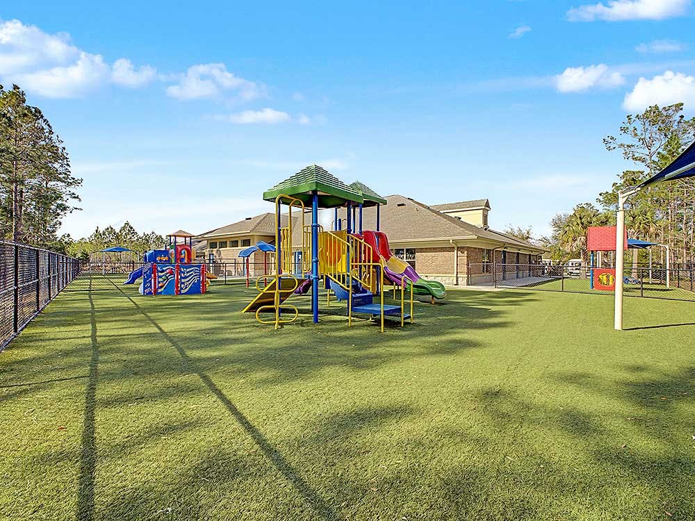 A large outdoor playground with multiple colorful slides and play structures on artificial turf