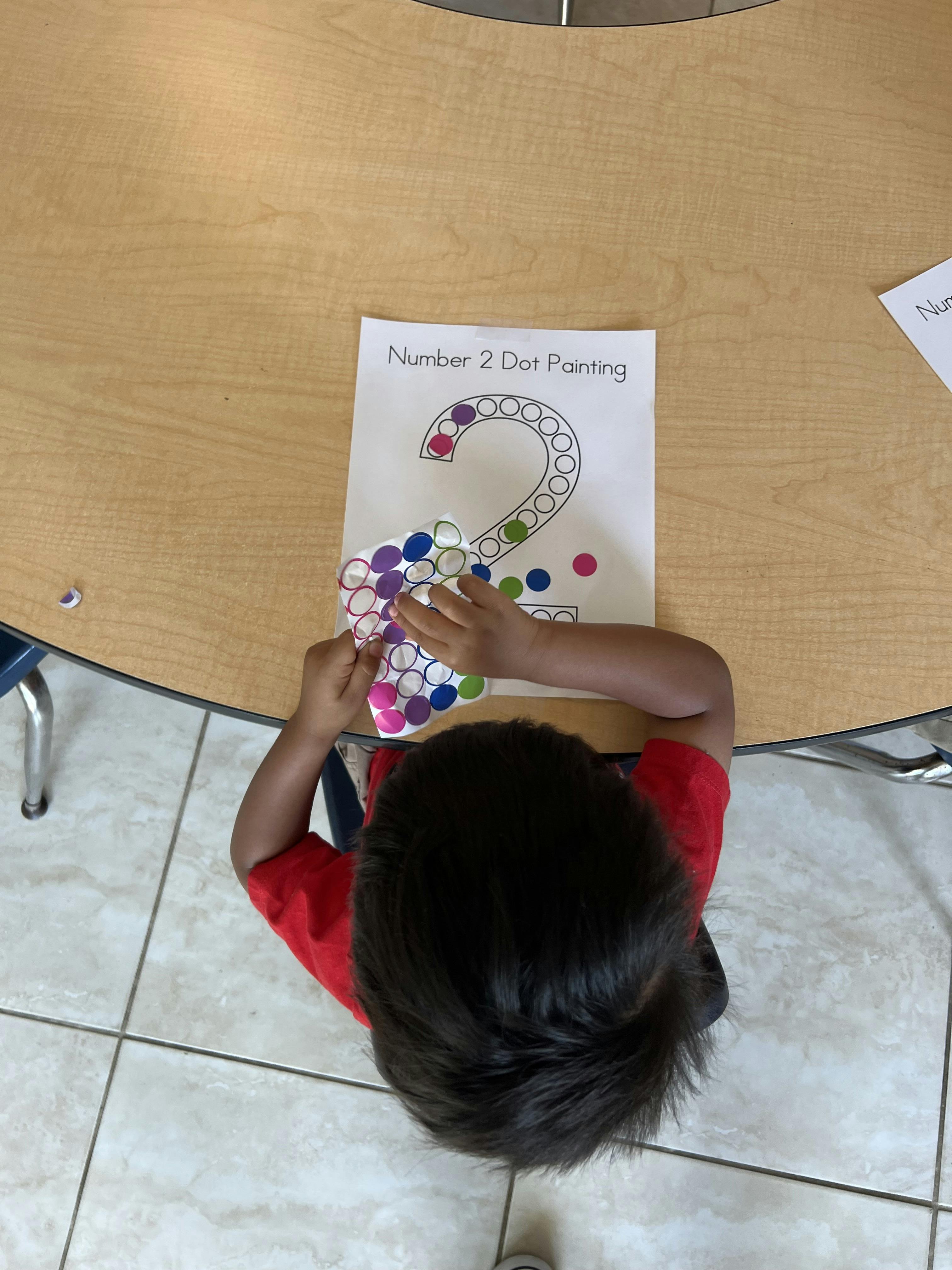 Child placing colorful stickers onto a paper with the number two