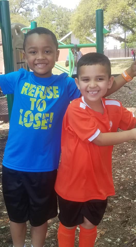 Two children smiling at the camera, one wearing a blue shirt with "REFUSE TO LOSE!"