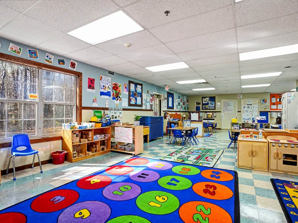 Colorful classroom with rugs, small tables, chairs, and shelves of learning materials