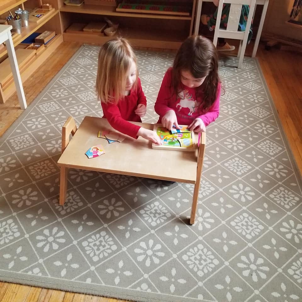 Two children playing with a puzzle at a small table