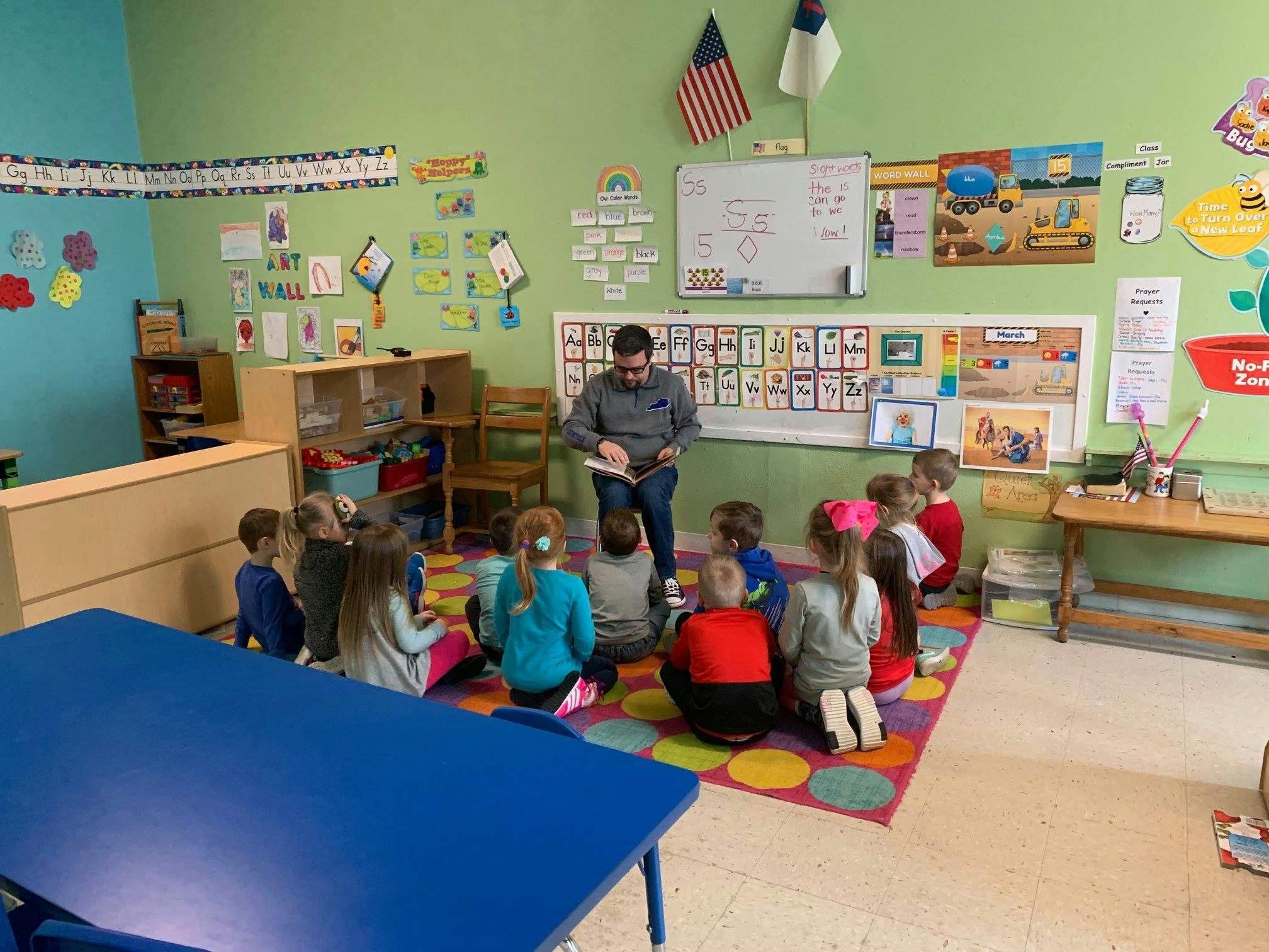 Adult reading a book to children sitting on a rug in a classroom