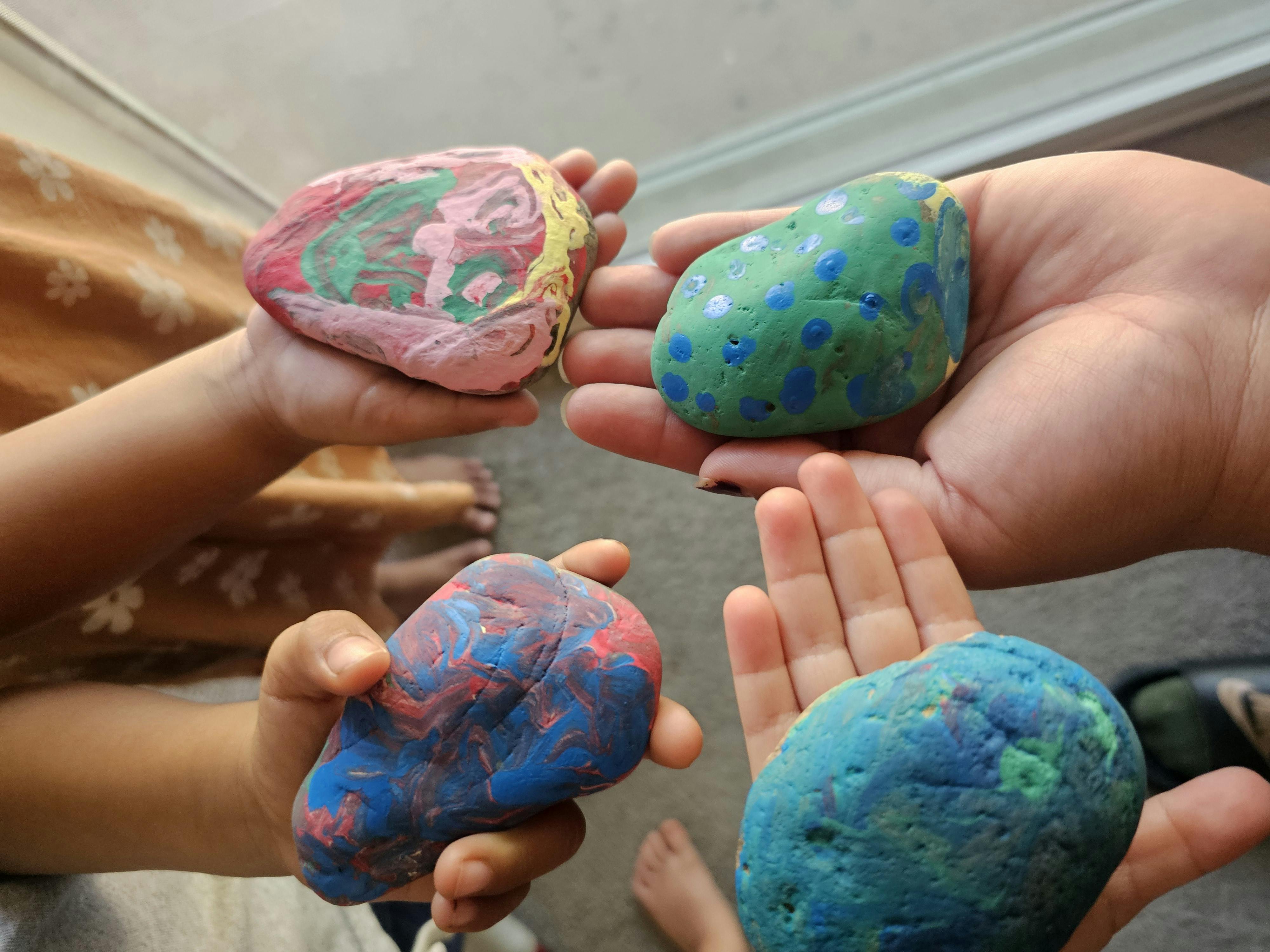 Multiple hands holding painted rocks