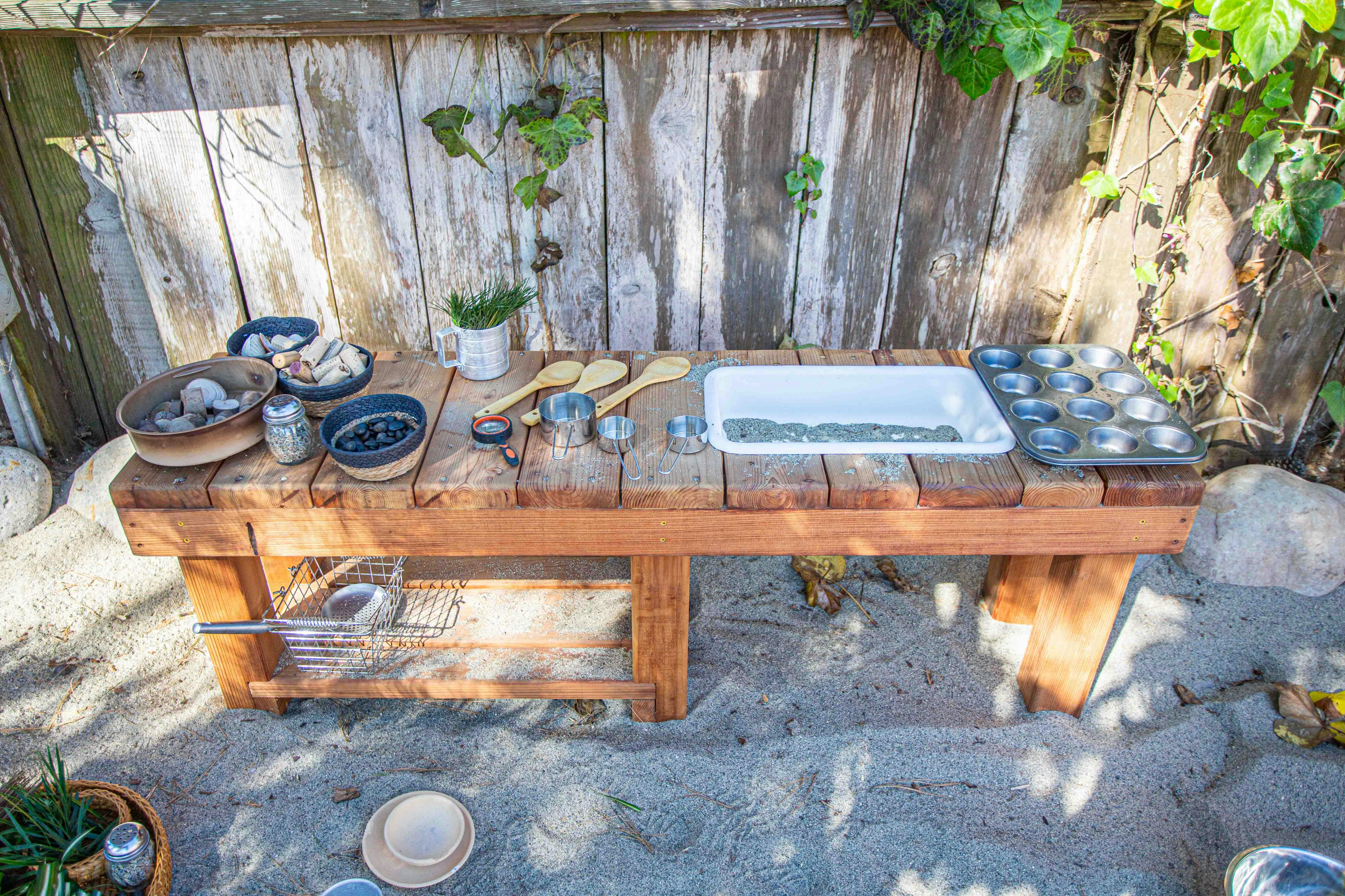 Outdoor wooden play kitchen with various pots, pans, and utensils