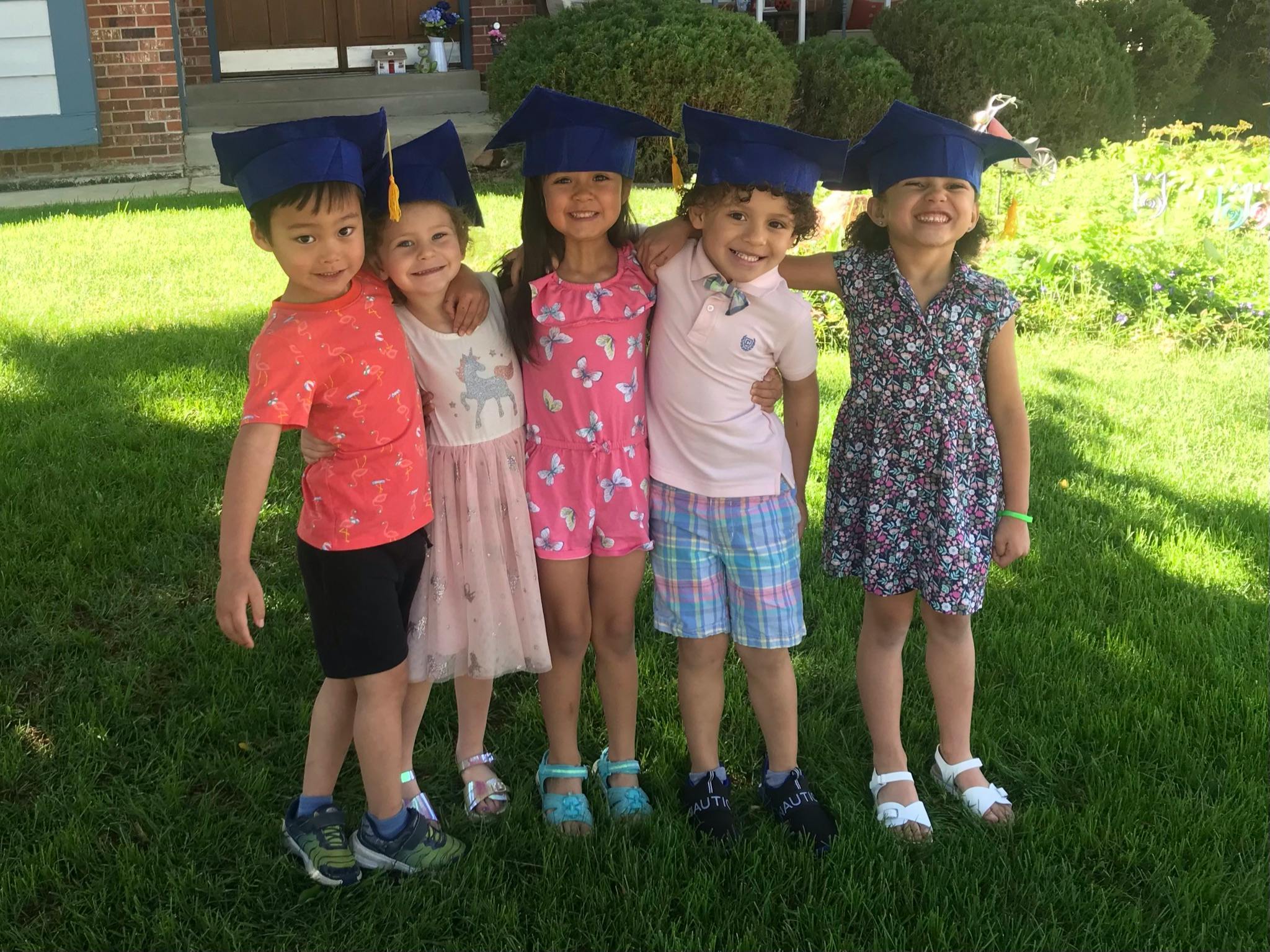 Five children wearing blue graduation caps, standing together on grass