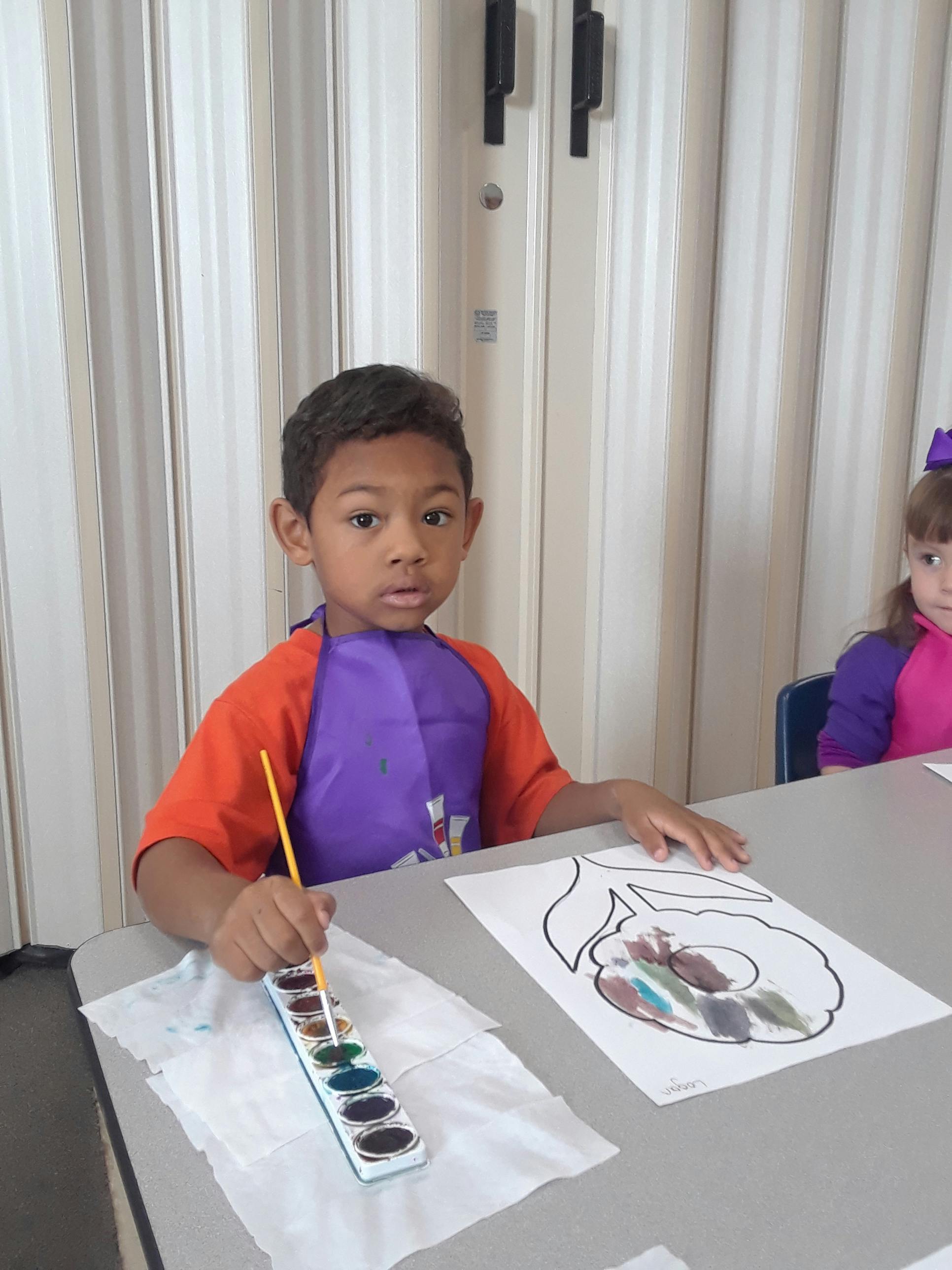 Child in an apron painting a picture at a table