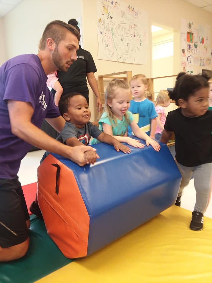 Adult and children playing with a large blue and orange foam block