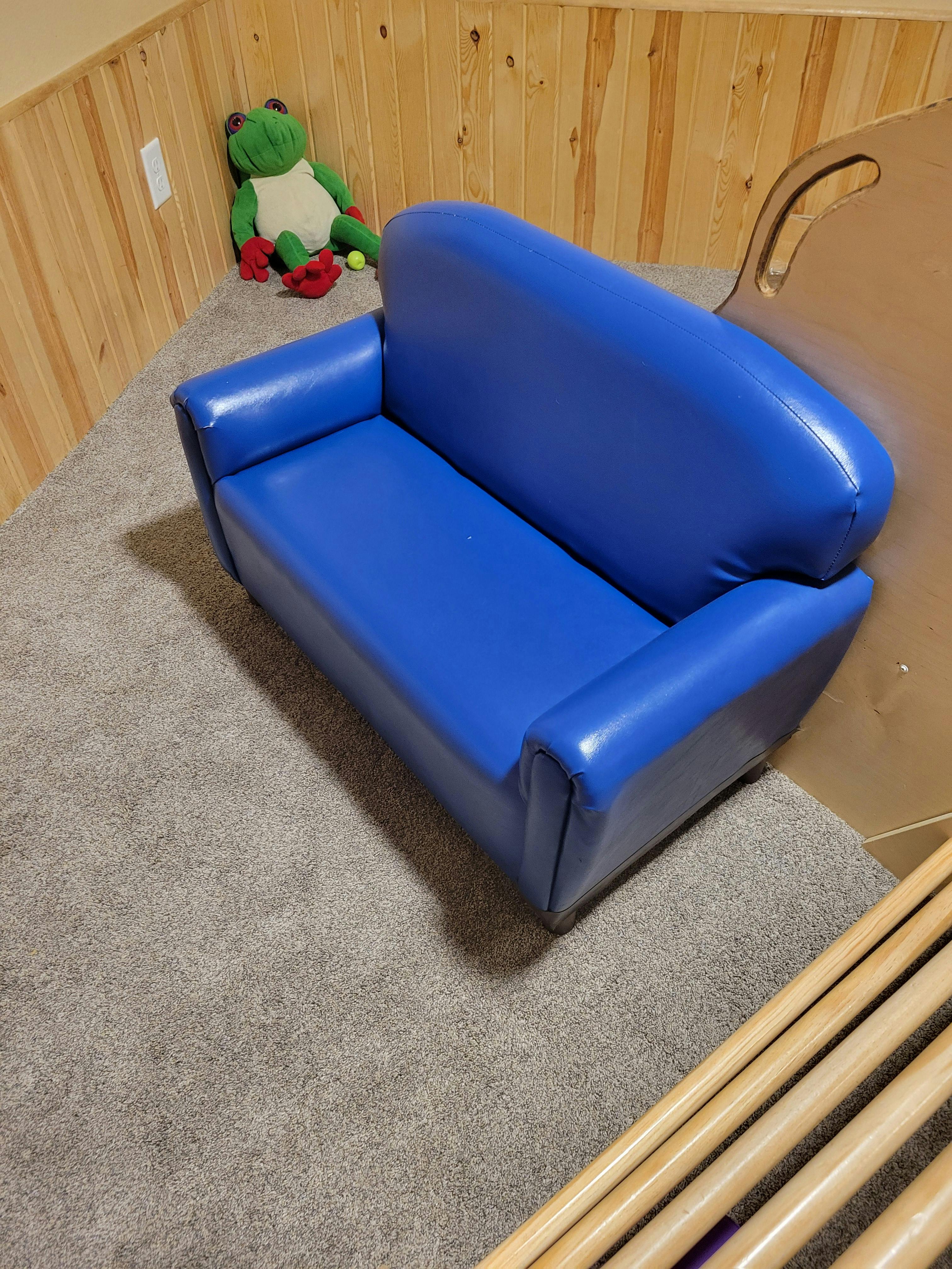 Blue child-sized sofa on carpet with a stuffed frog in the background