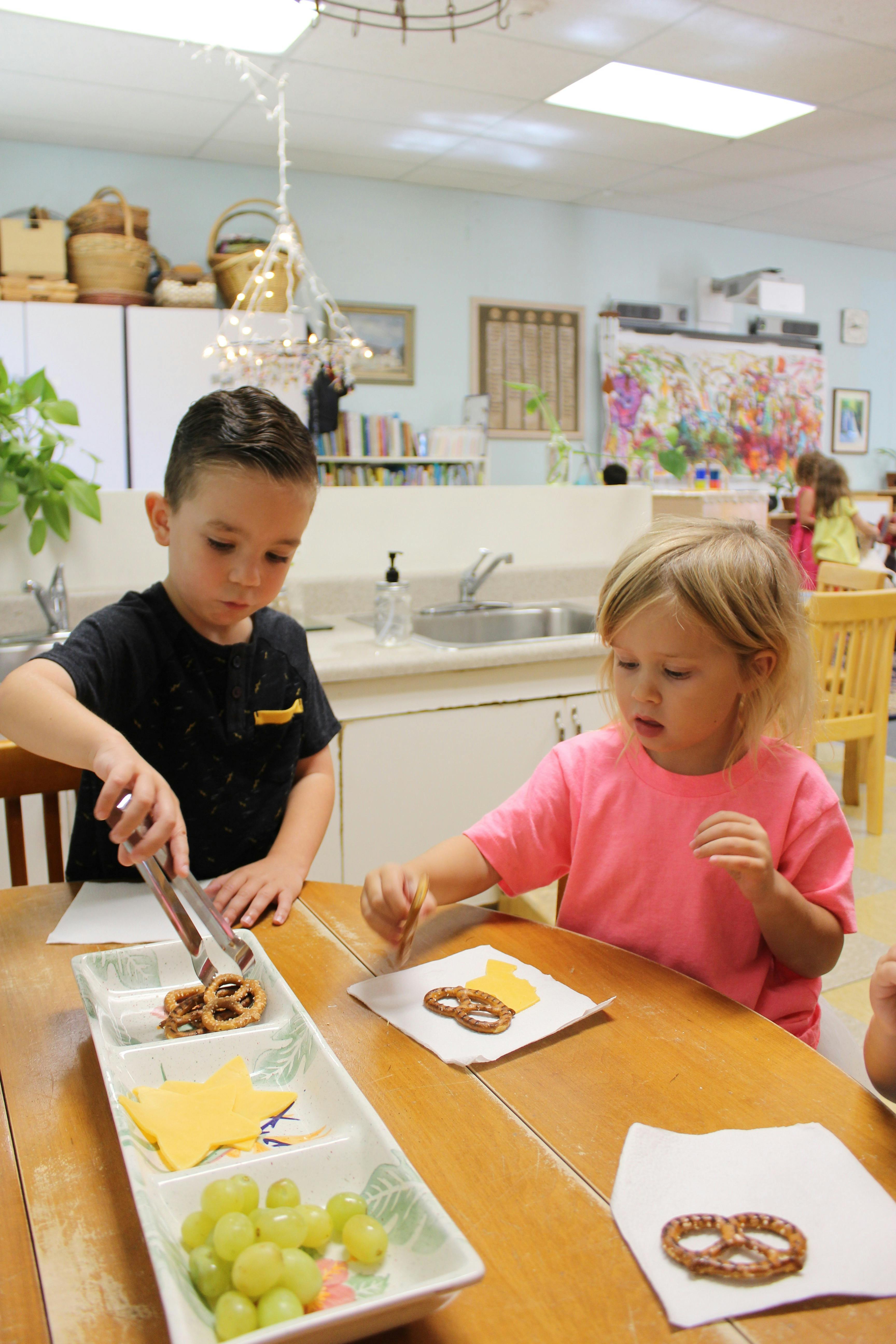 Child using tongs to pick up a pretzel from a snack tray
