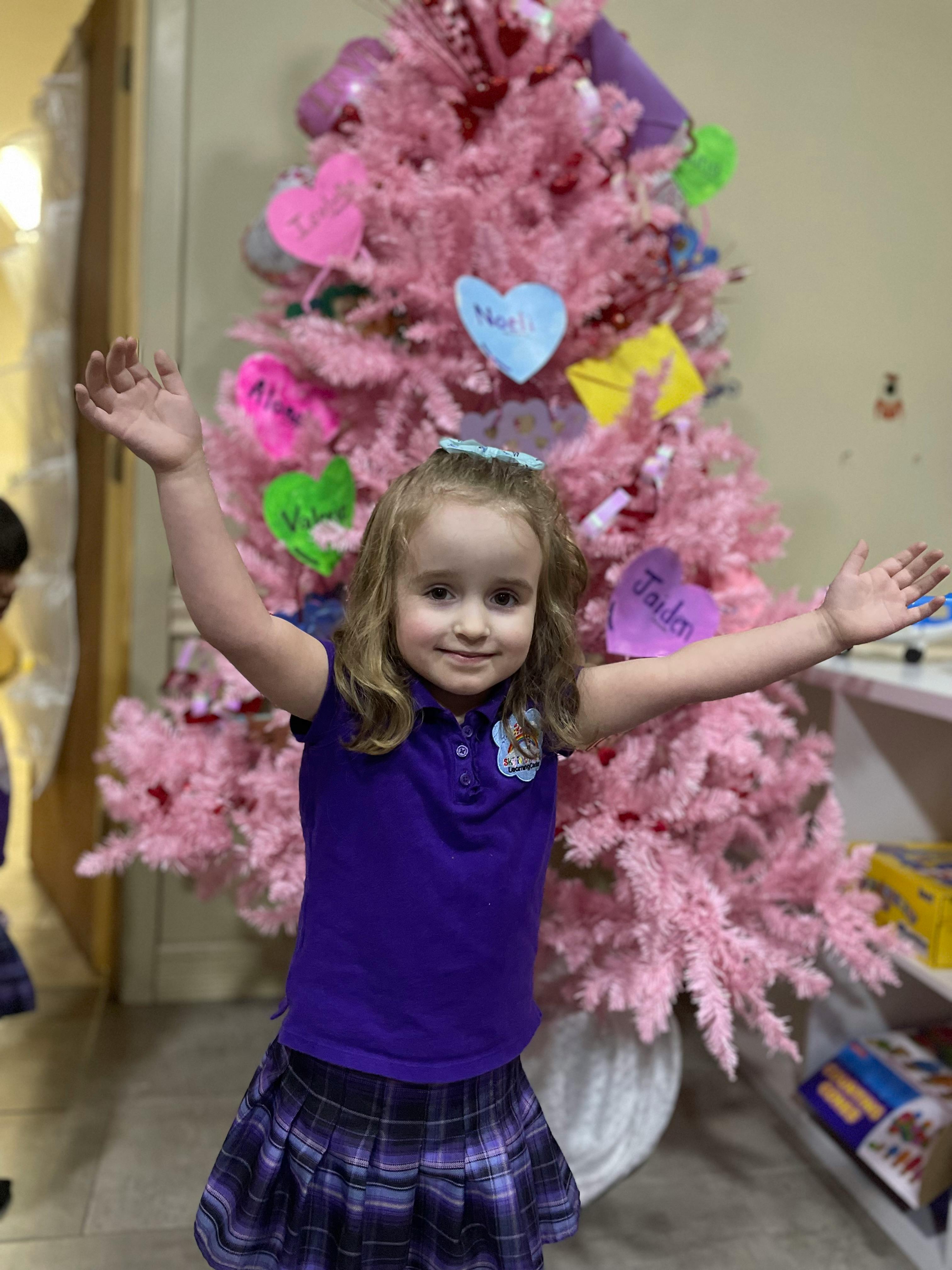 Child with arms raised in front of a pink decorated tree