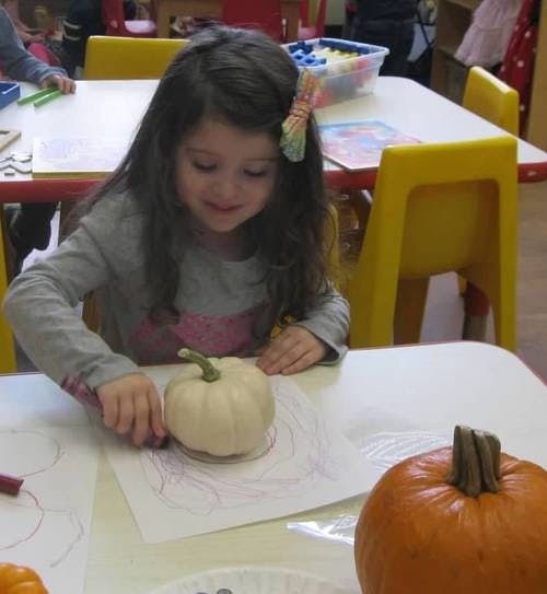 Child drawing on paper with a small white pumpkin on the table