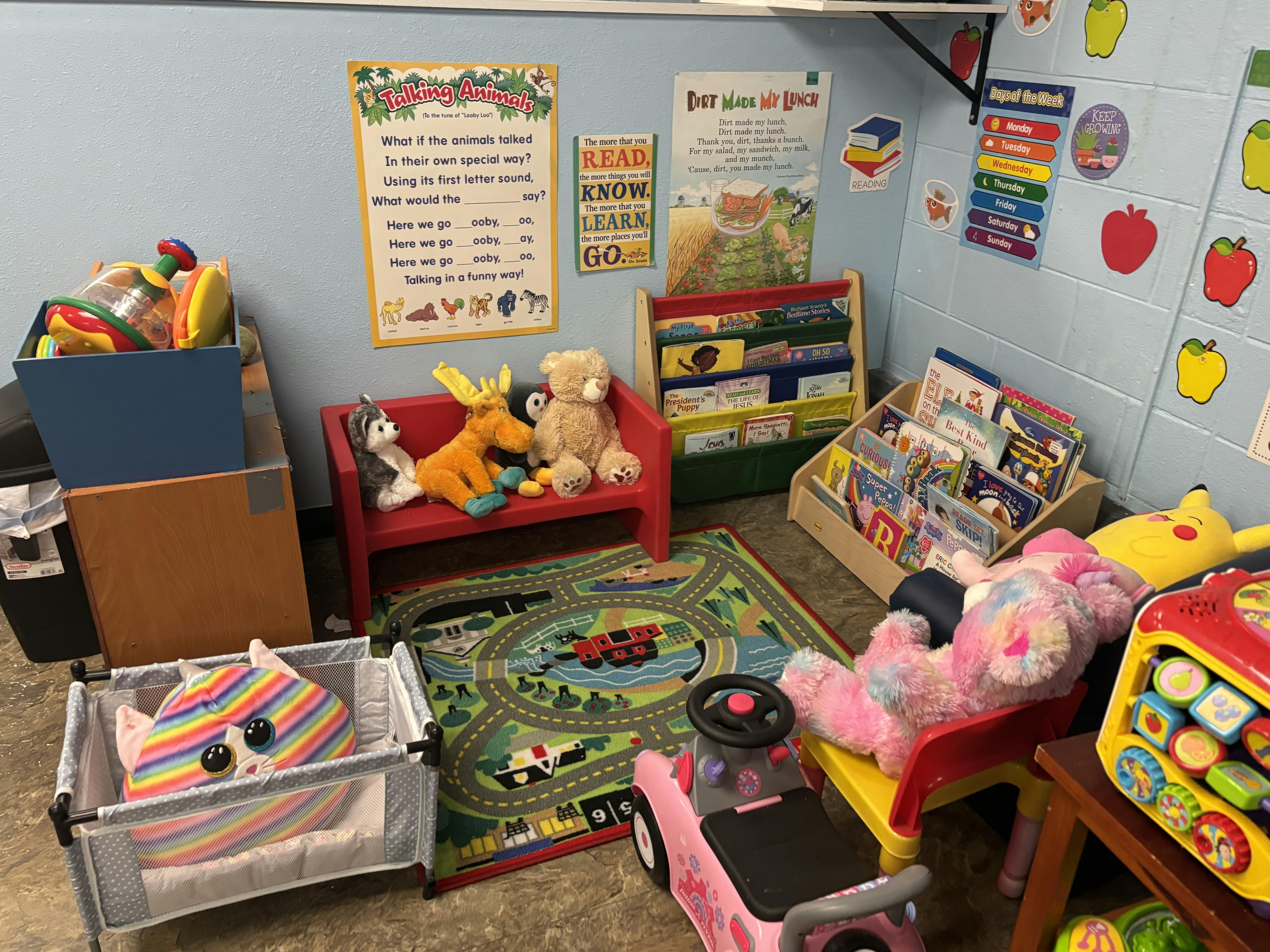 Classroom corner with books, posters, plush toys on a bench, and ride-on toys