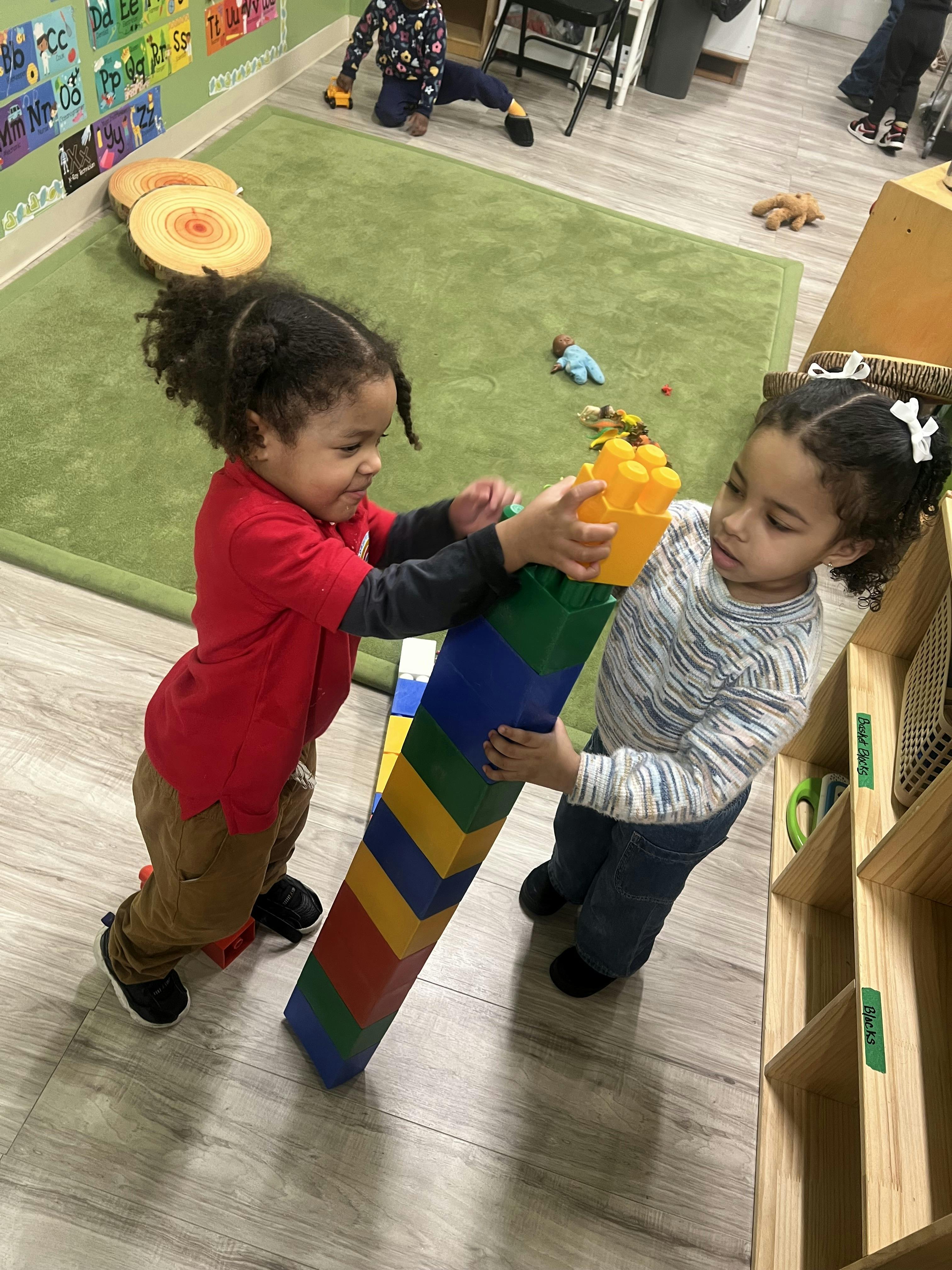 Two children playing with large colorful building blocks in a classroom