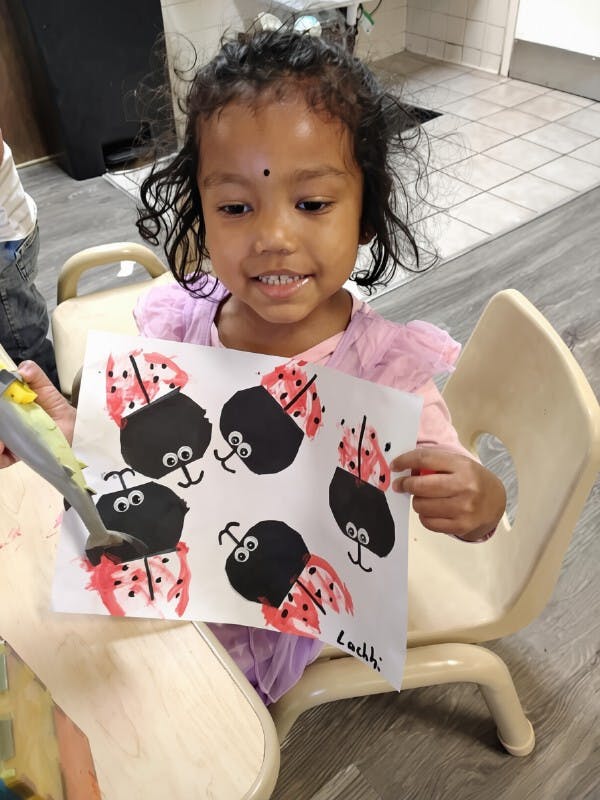 Child holding a paper with hand-painted ladybug illustrations