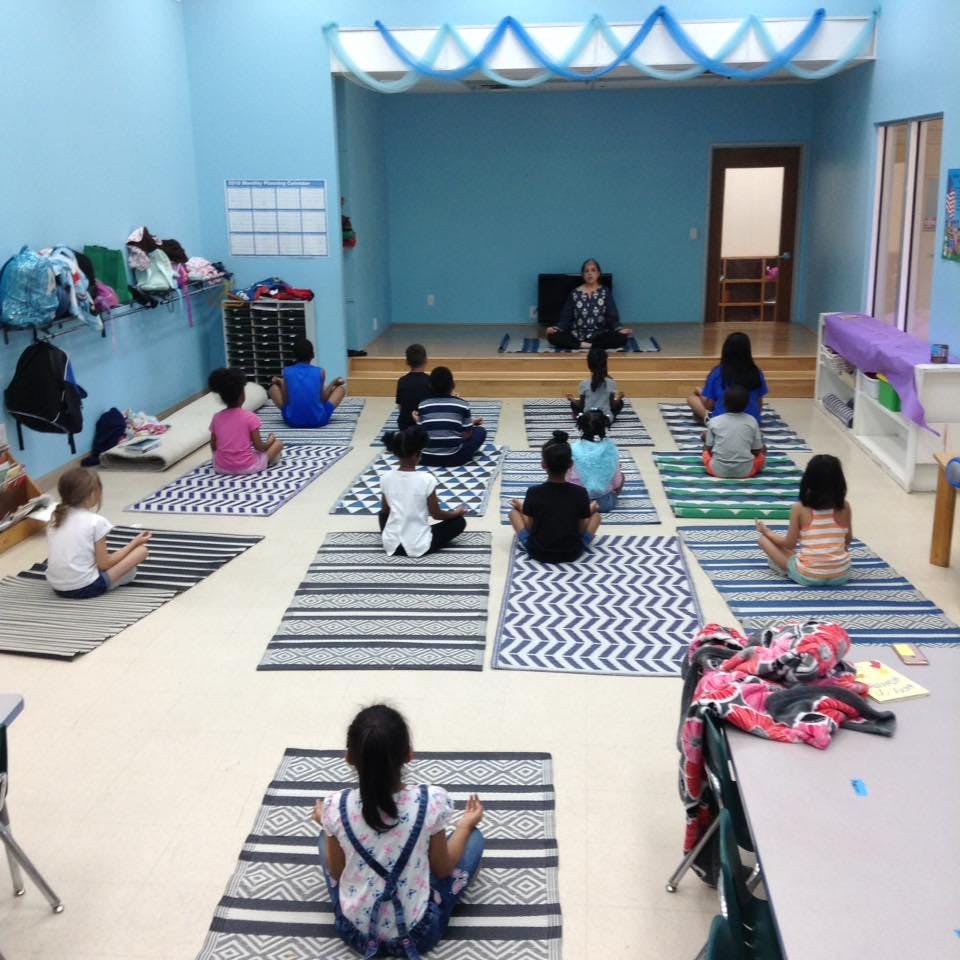 Children and an adult sitting on yoga mats in a classroom
