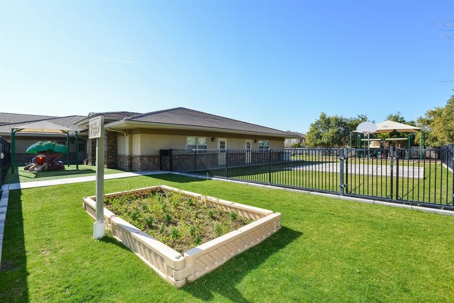 Building exterior with a fenced playground and a raised garden bed