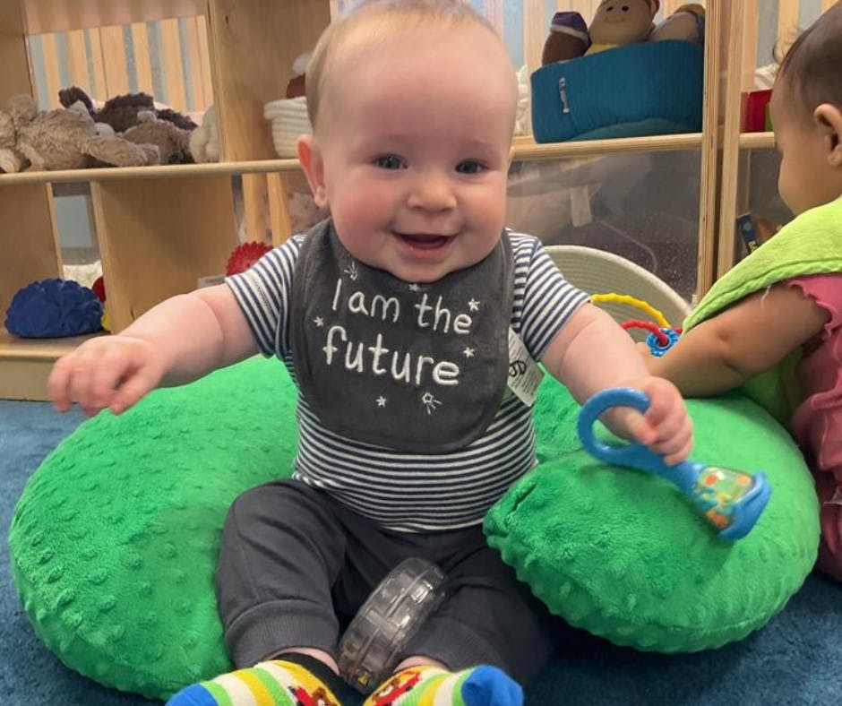 Child sitting on a green cushion wearing a bib that says "I am the future"