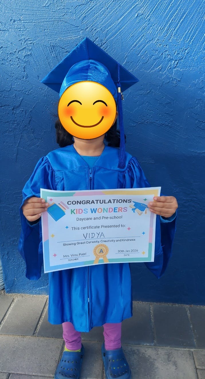 Child in a blue graduation cap and gown holding a certificate that reads "Kids Wonders"