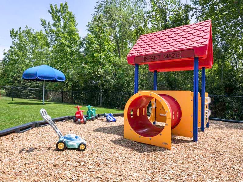 A toddler playground with a tunnel, toy lawnmower, and riding toys