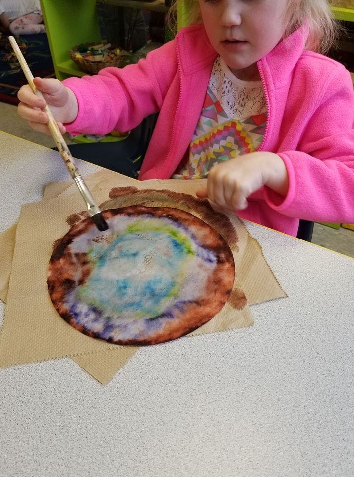 Child painting a circular paper craft with a brush